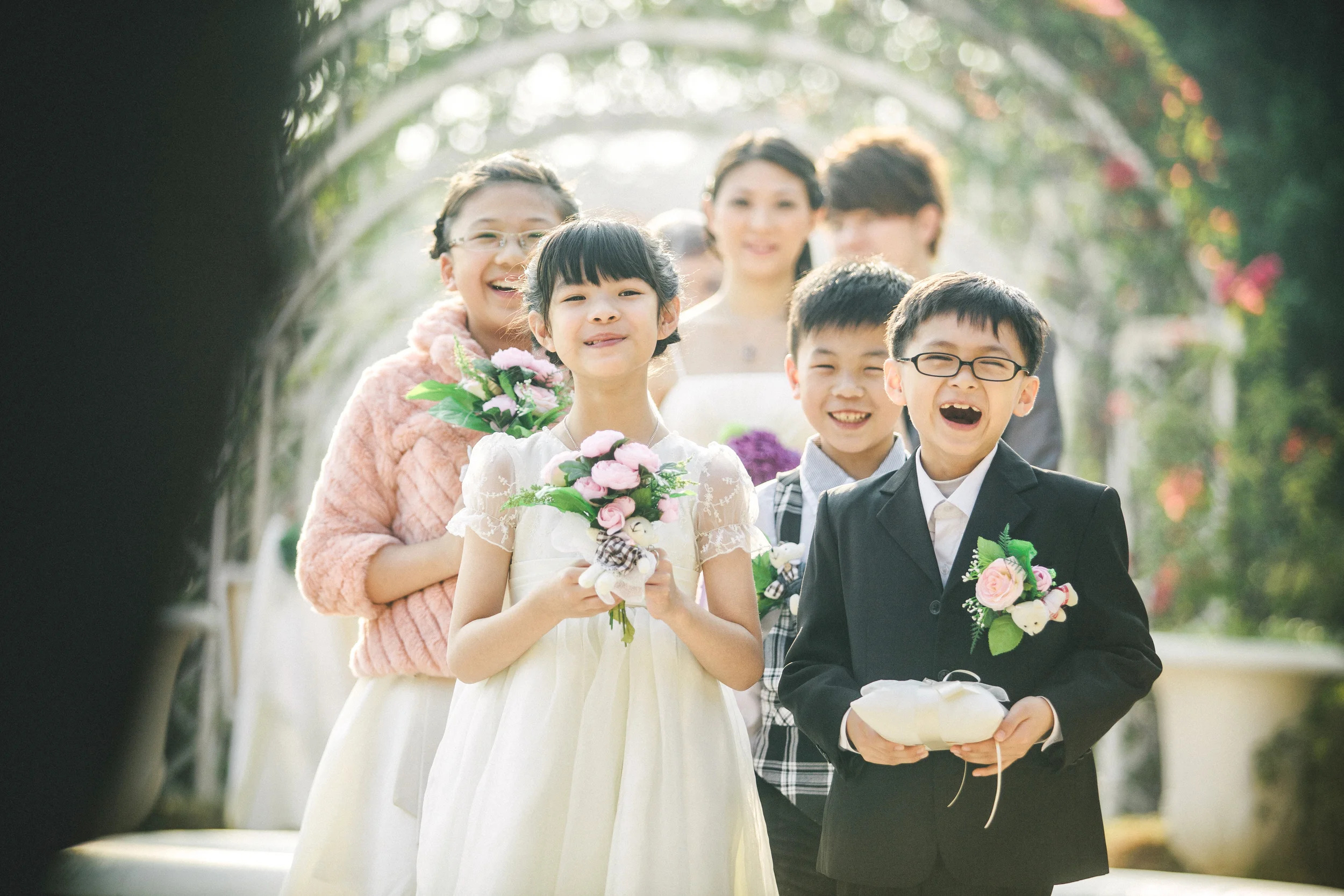 Wedding couple smiling with family beneath a leafy archway.