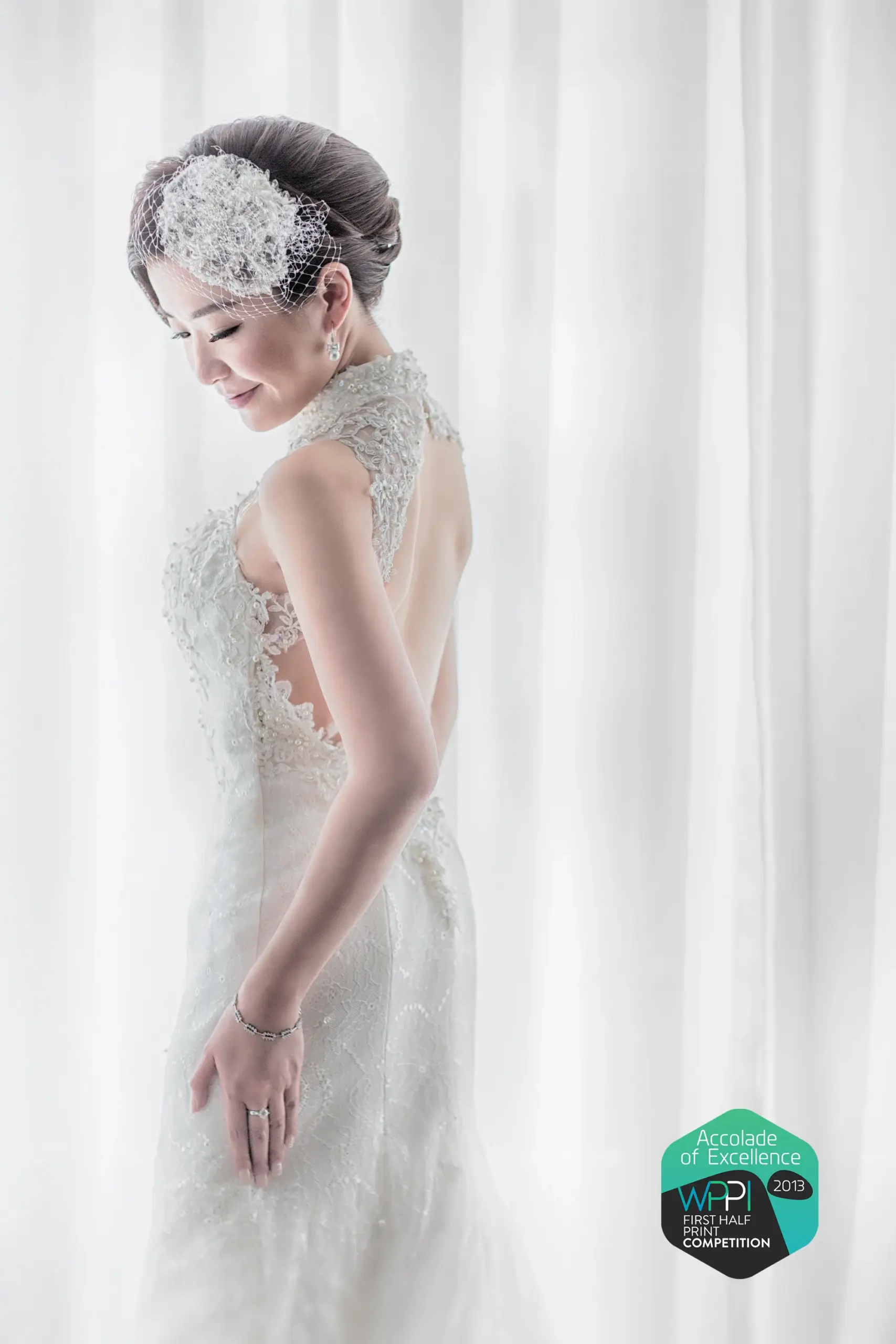 Bride in a floral lace gown beside a bright window, with a WPPI award badge.