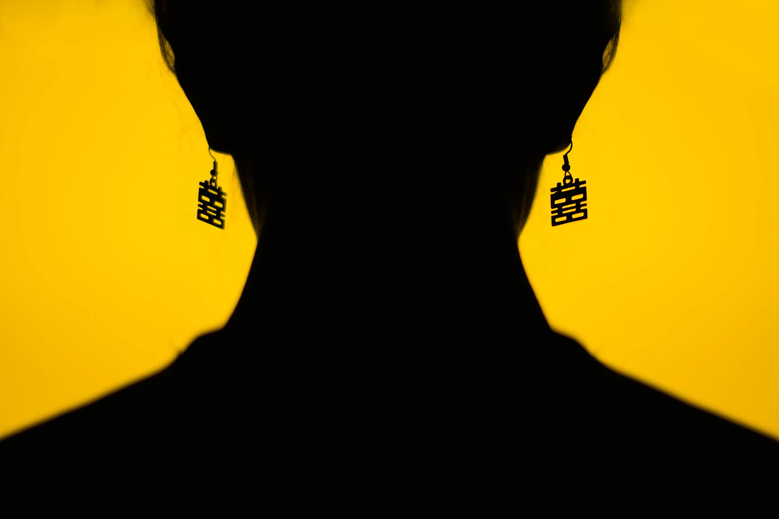 Two silhouetted figures against a yellow backdrop bearing double-happiness characters.