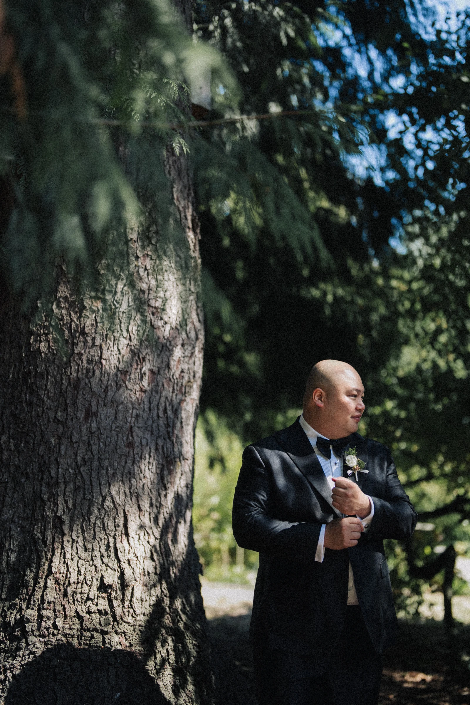 Groom standing beside a broad tree trunk in the shade at Paulik Park.