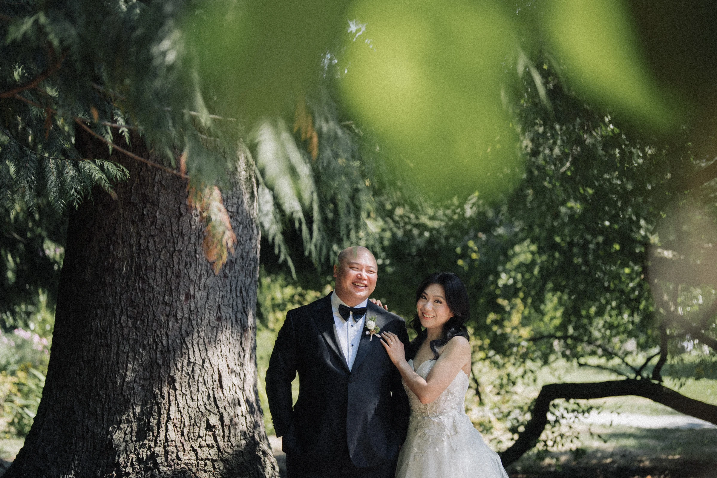 Bride and groom standing close beside a tree at Paulik Park.
