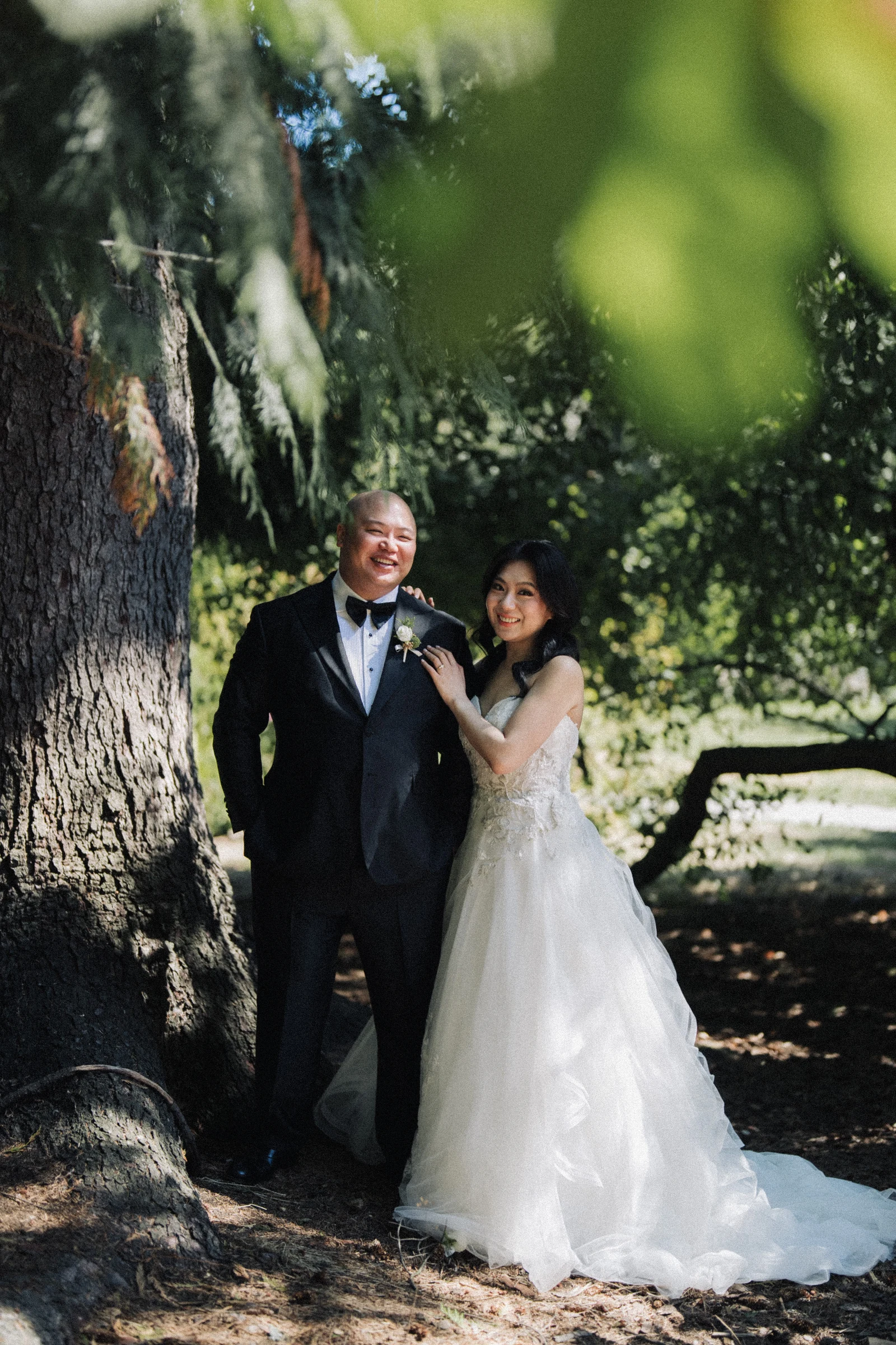 Full-length portrait of the couple beside the tree, with the wedding dress spread below.