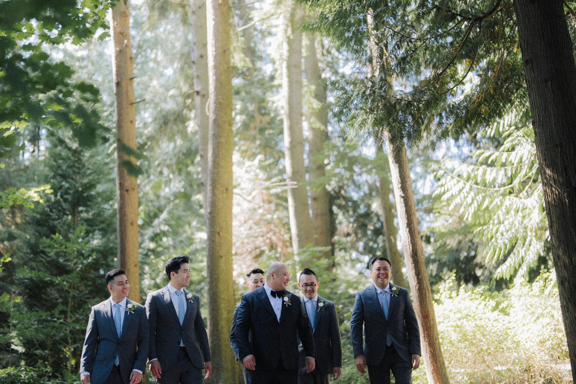 Groomsmen walking together between the tree trunks.