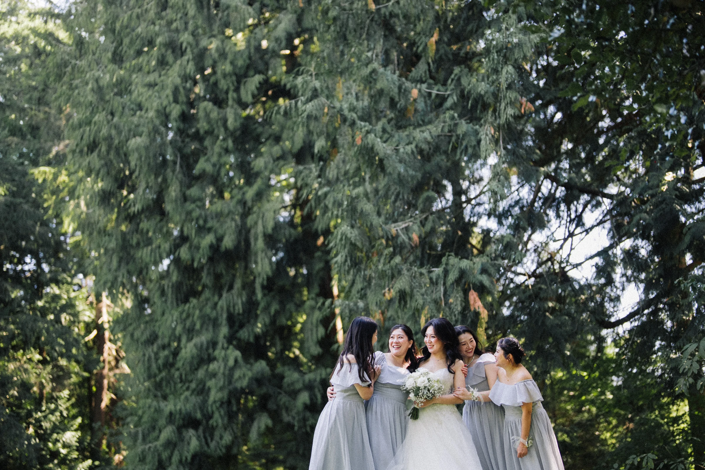 Bridesmaids leaning together around the bride in the park.