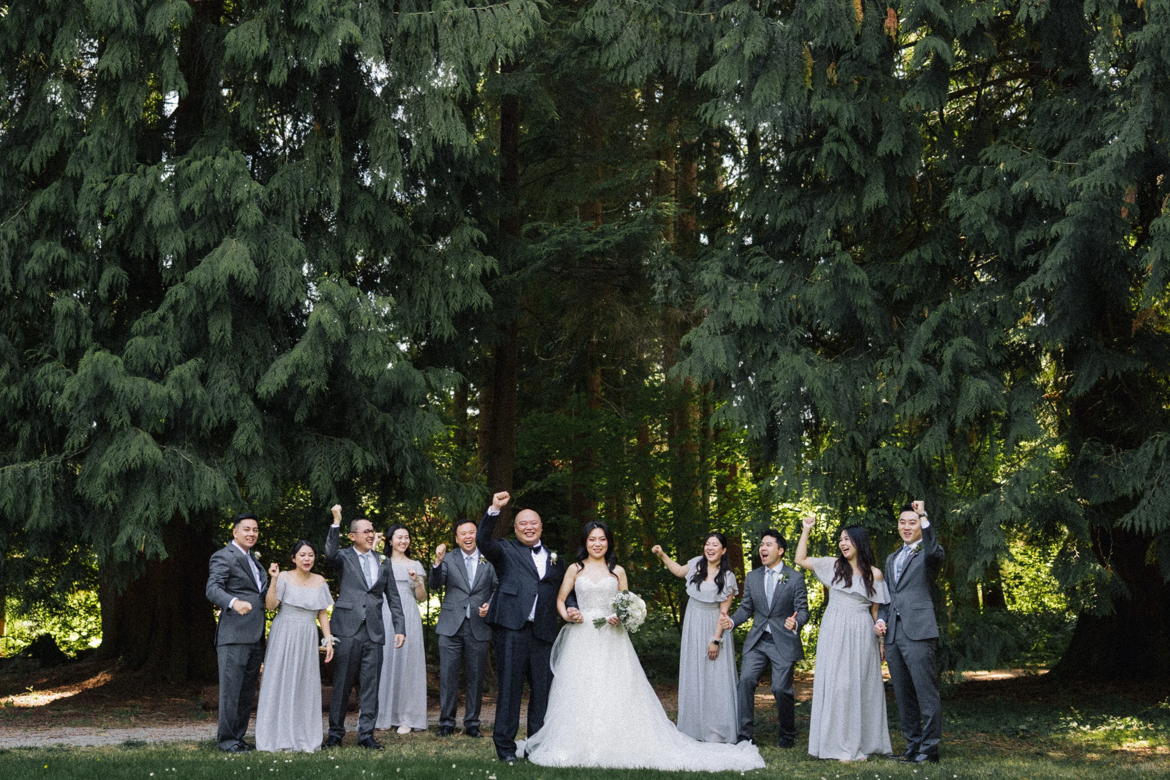 Bride and groom standing at the centre of the wedding party in the shade.