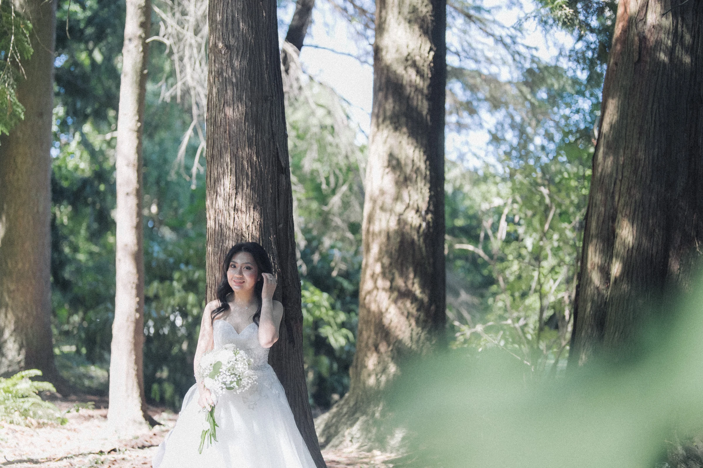 Bride standing against a tree with soft green leaves in the foreground.