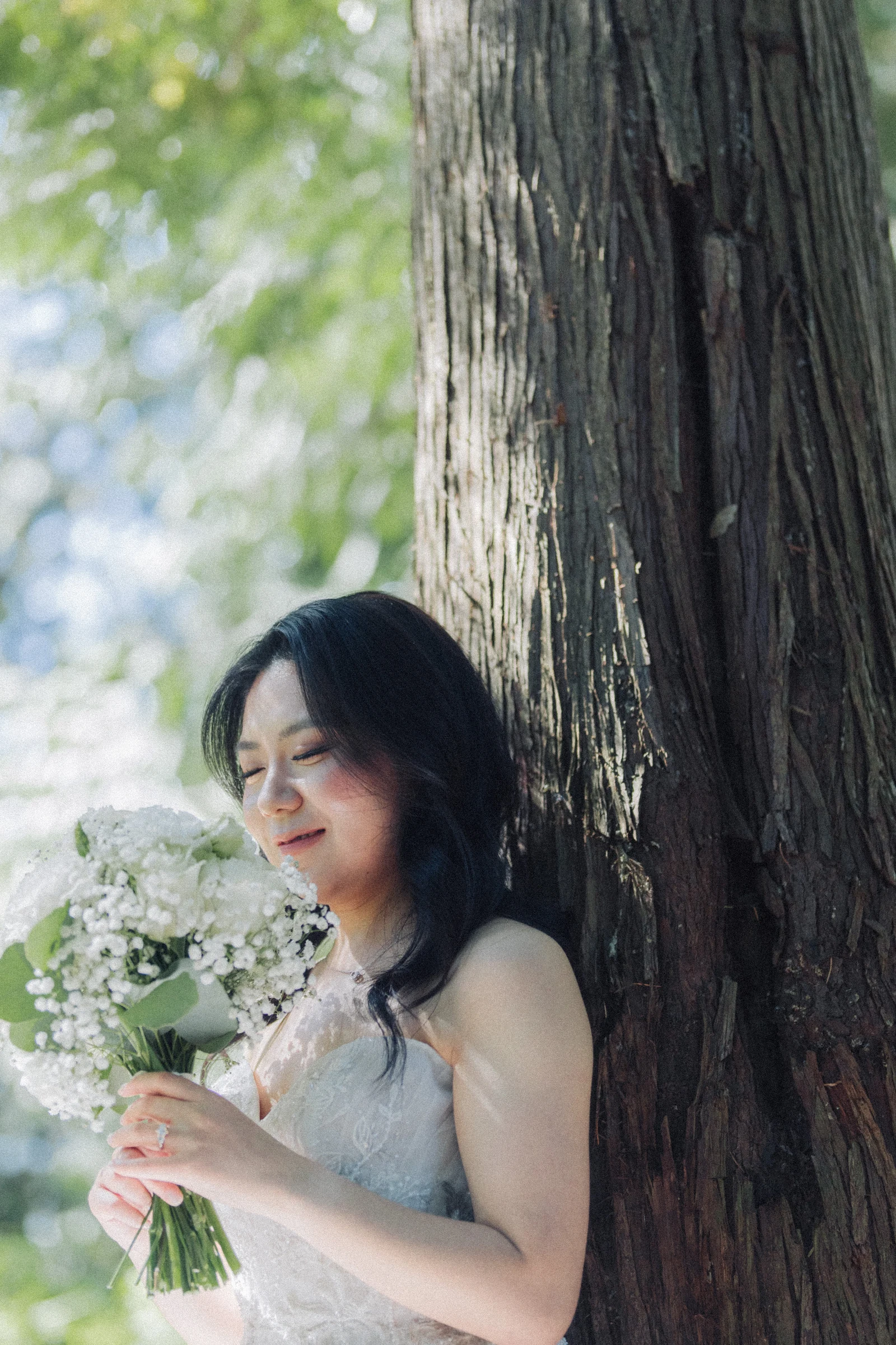 Bride holding her bouquet beside a textured tree trunk.