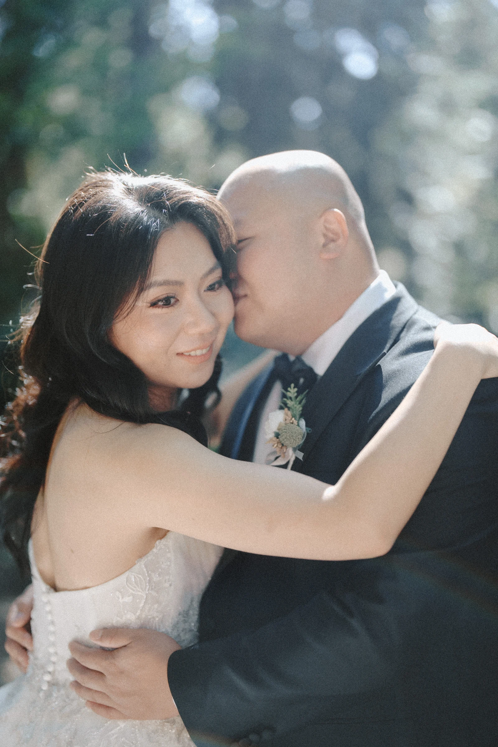 Groom kissing the bride's temple as she holds him close.