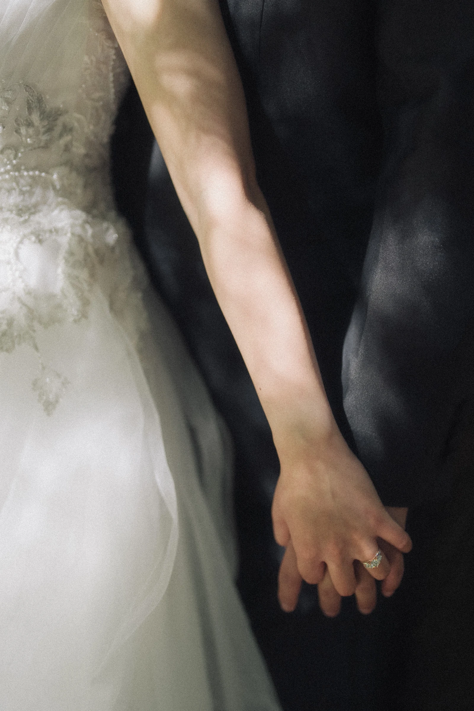 Detail of the couple's joined hands beside the wedding dress.
