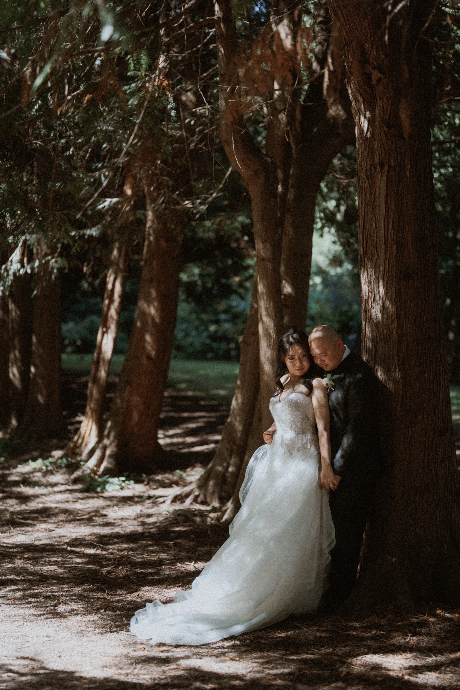Couple resting together beside a tree, with the wedding dress spread below.