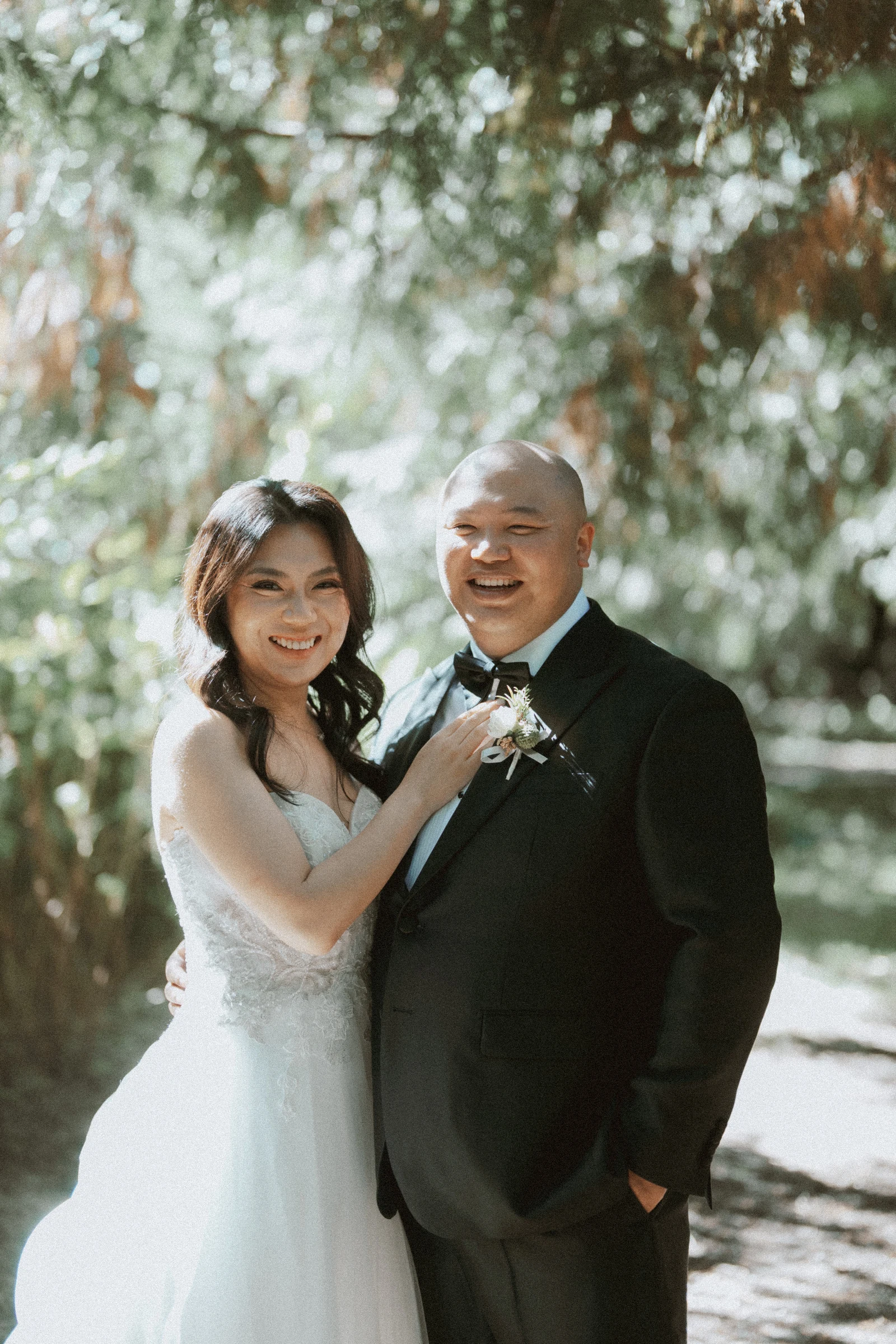 Couple laughing together beneath a bright woodland canopy.