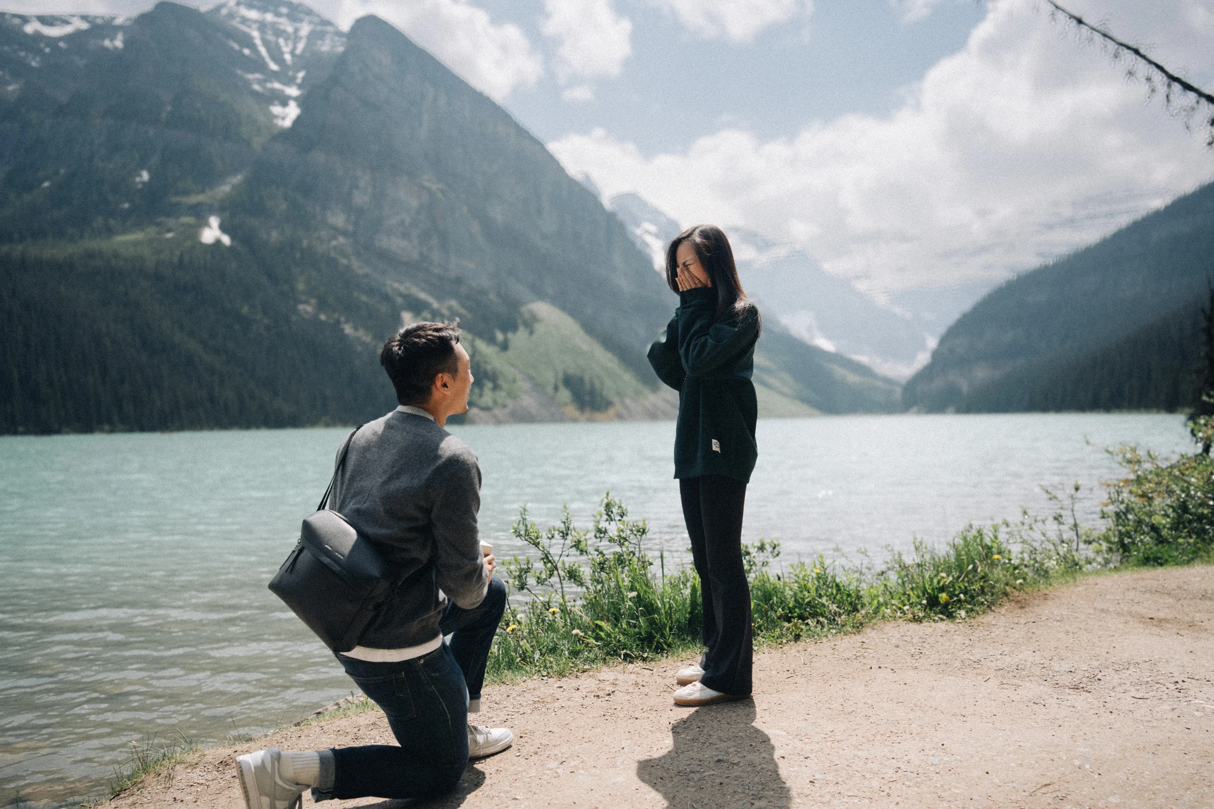 Proposal photography at Lake Louise in Banff National Park: Desmond kneels in front of Rachael on the path beside Lake Louise.