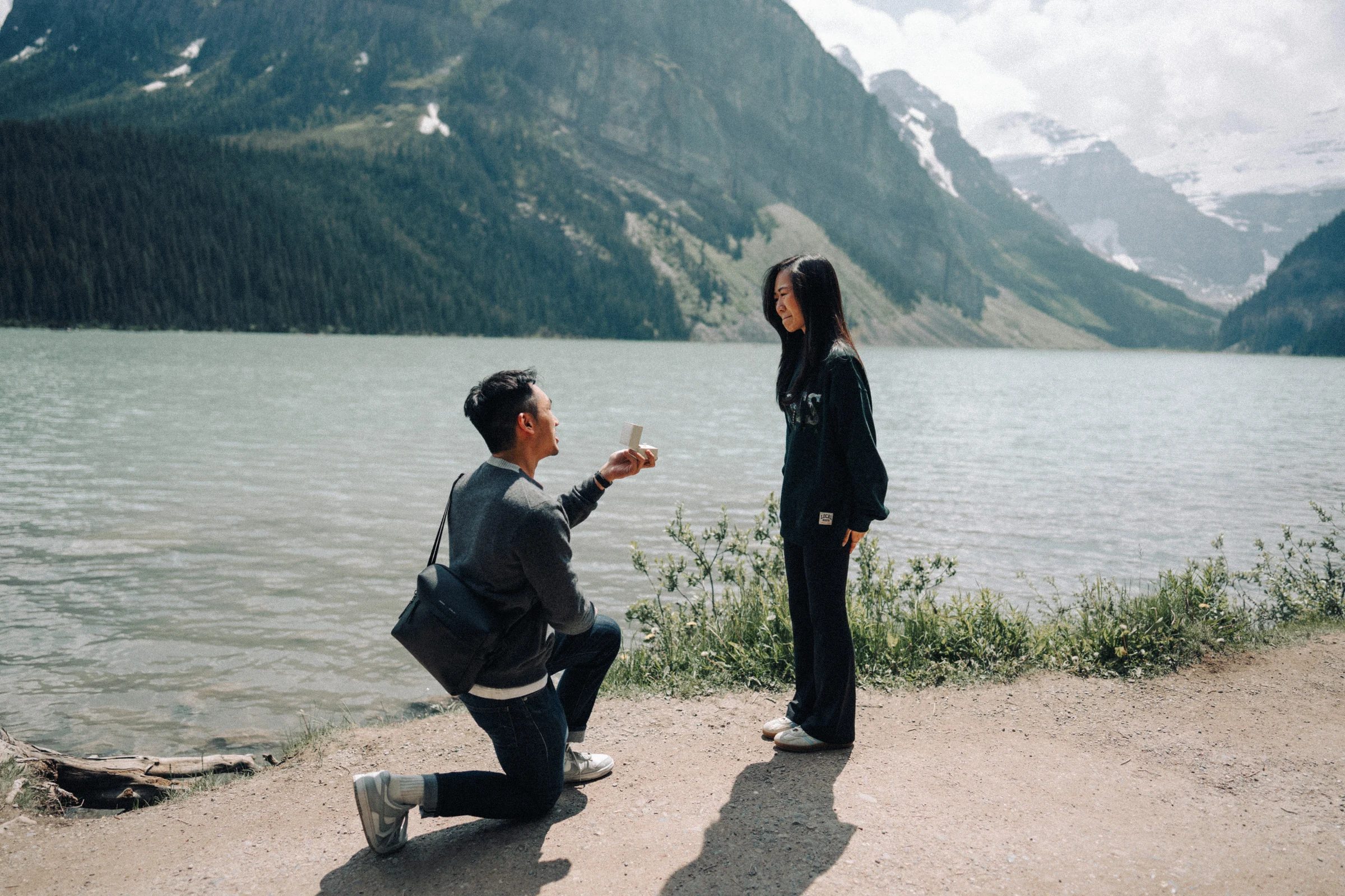 Proposal photography at Lake Louise in Banff National Park: Desmond holds out a ring while kneeling beside Rachael at the lake.