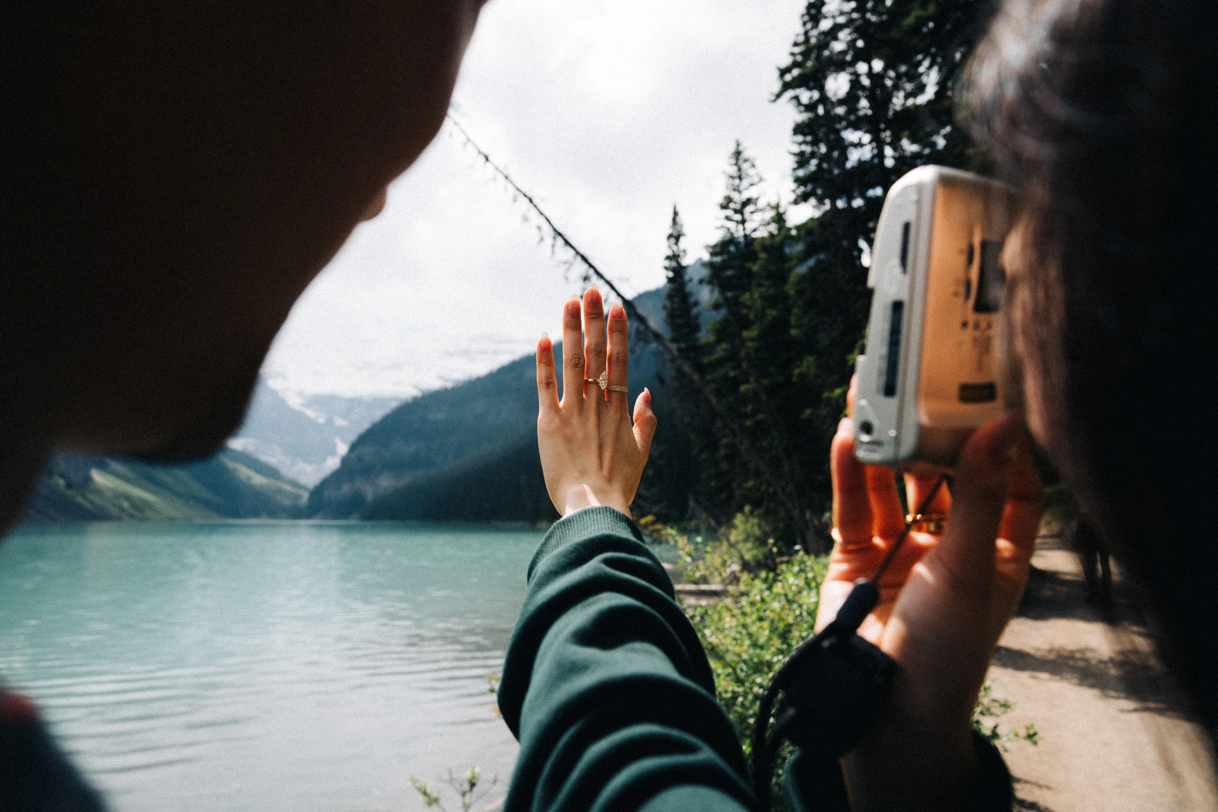 Rachael holds up her ring hand as an instant camera photographs it beside Lake Louise in Banff National Park.