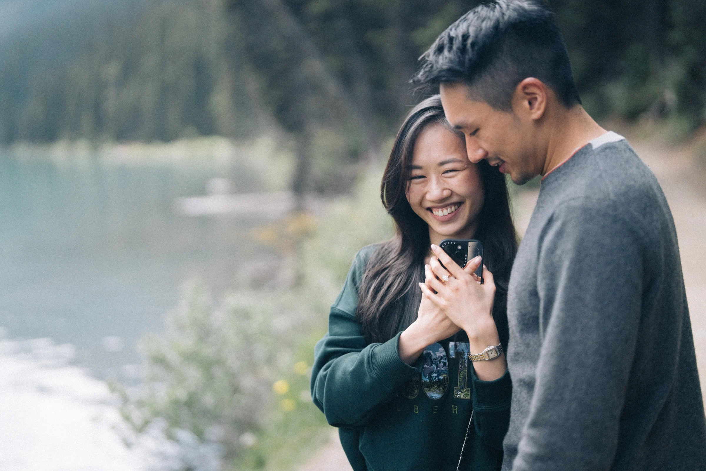 Rachael smiles and holds up her ring hand beside Desmond, at Lake Louise in Banff National Park.