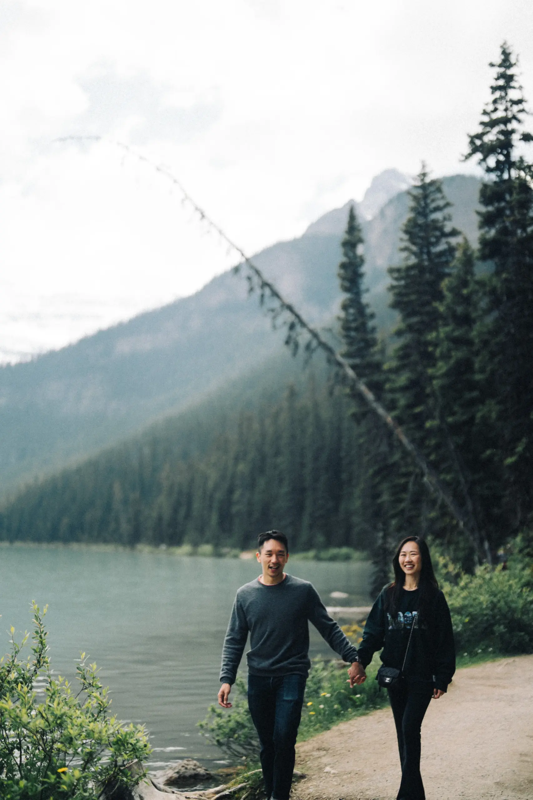 Rachael and Desmond walk hand in hand on the path beside Lake Louise in Banff National Park.