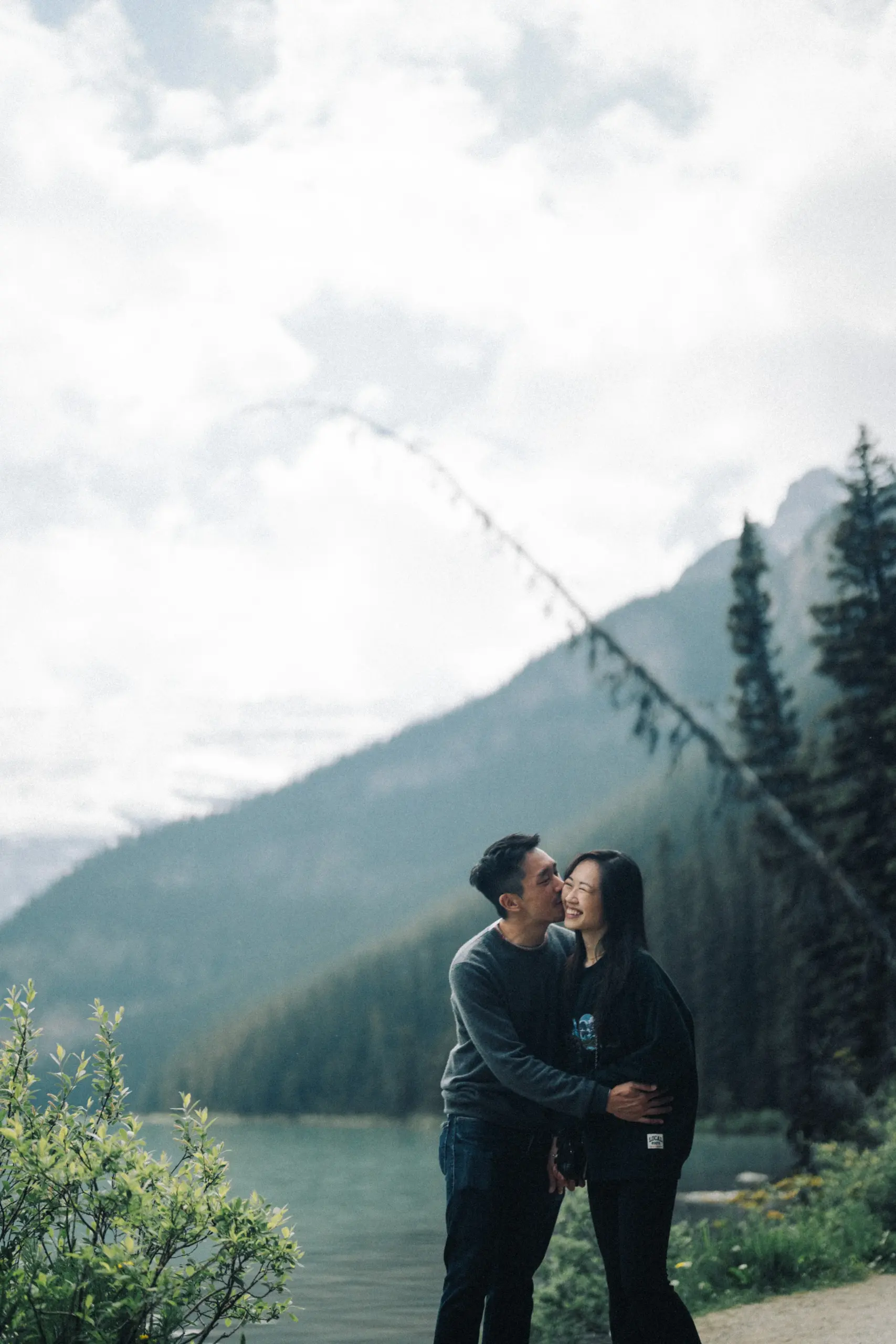 Rachael and Desmond kiss beneath a tree beside Lake Louise in Banff National Park.
