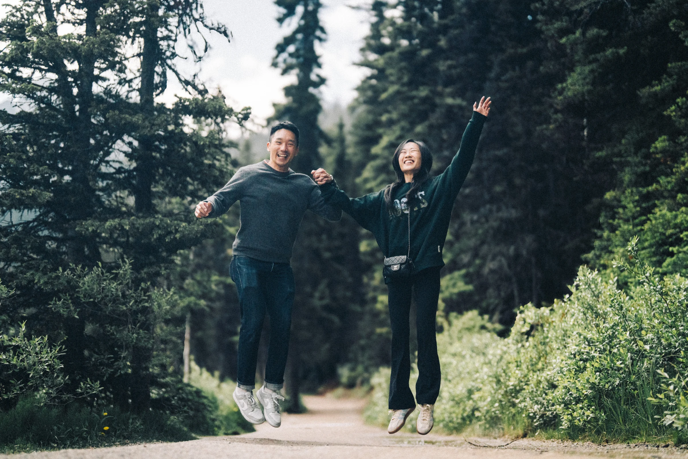 Rachael and Desmond jump together on the forest path beside Lake Louise in Banff National Park.