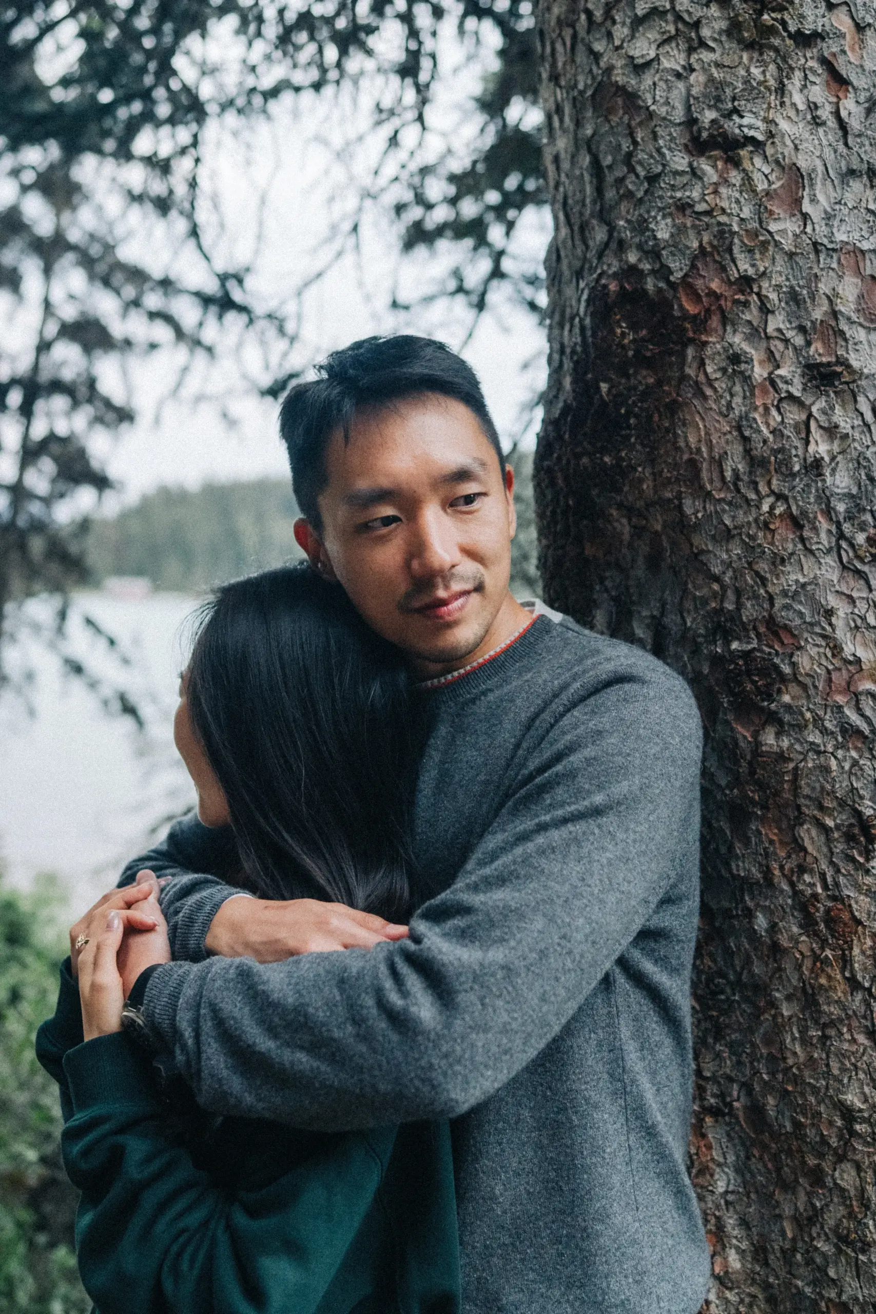 Desmond looks toward the camera while holding Rachael beside a tree, at Lake Louise in Banff National Park.