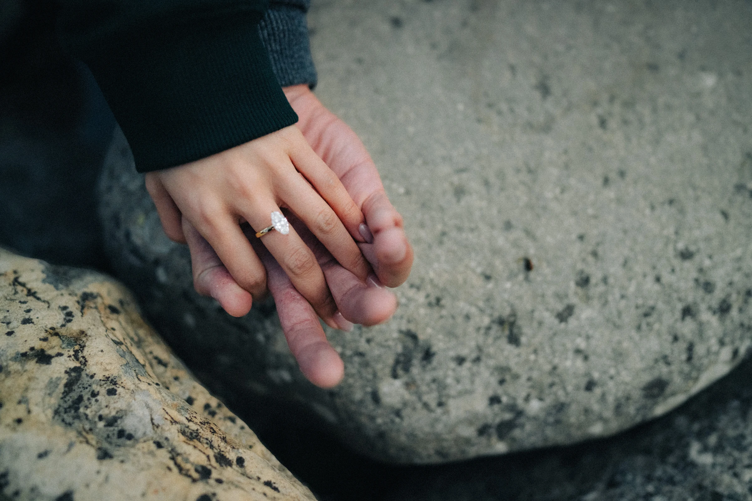 Close view of Rachael’s ring hand resting over Desmond’s hand on a rock, at Lake Louise in Banff National Park.