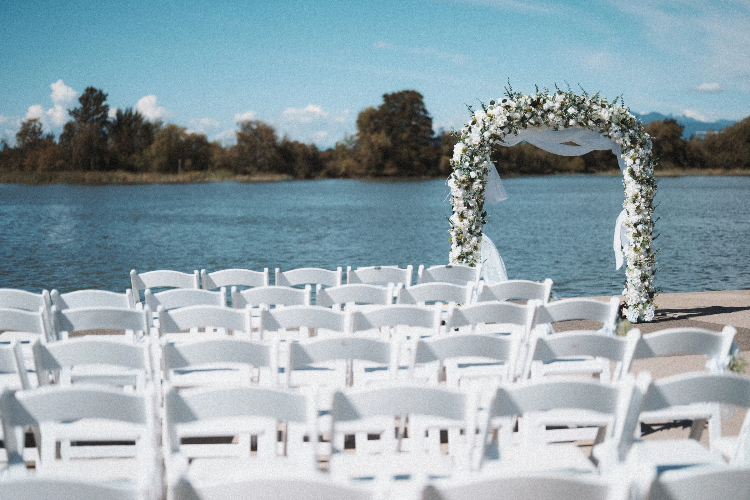 White ceremony chairs and a flower arch facing the Fraser River.