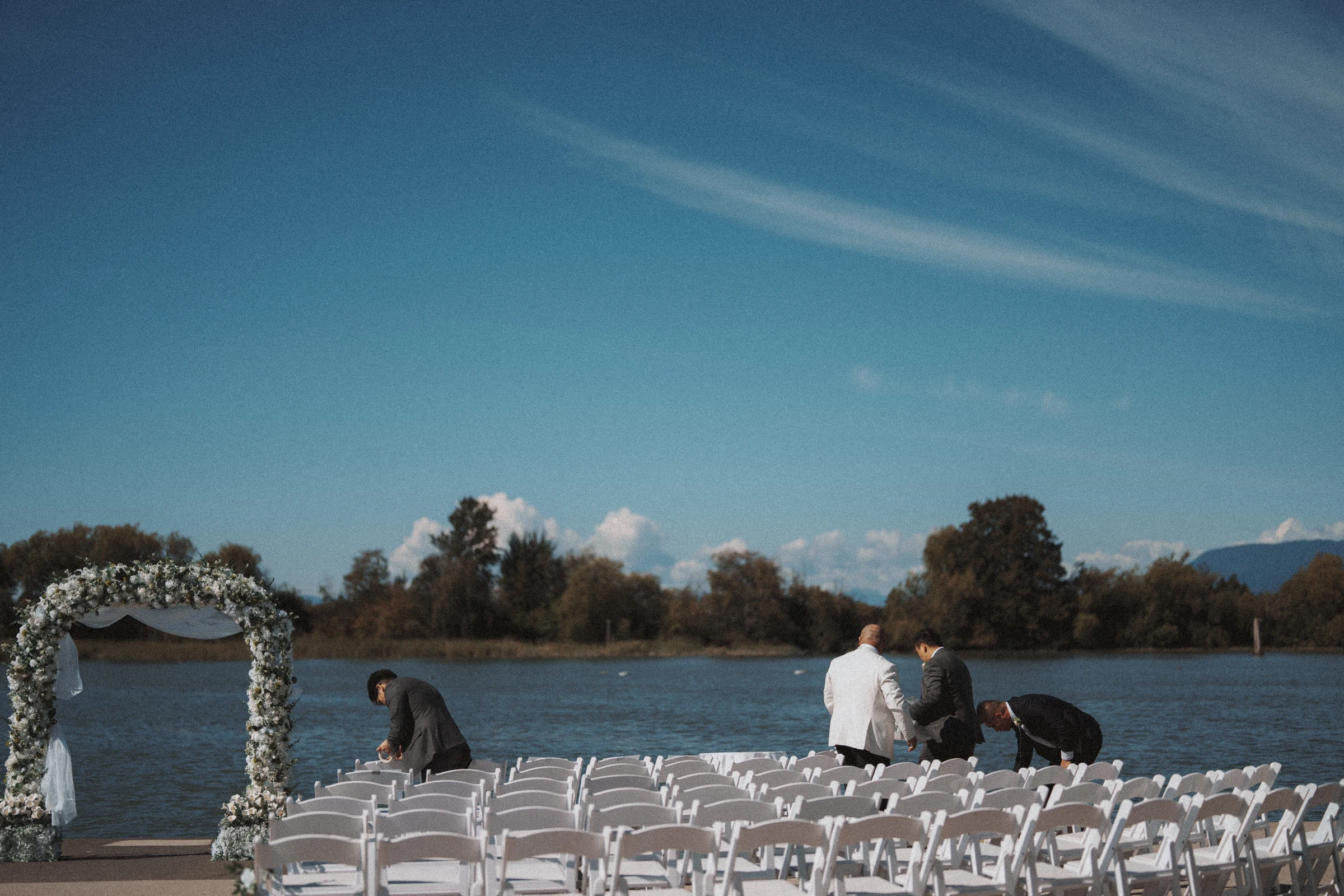 People preparing the waterfront ceremony seating beneath the flower arch.