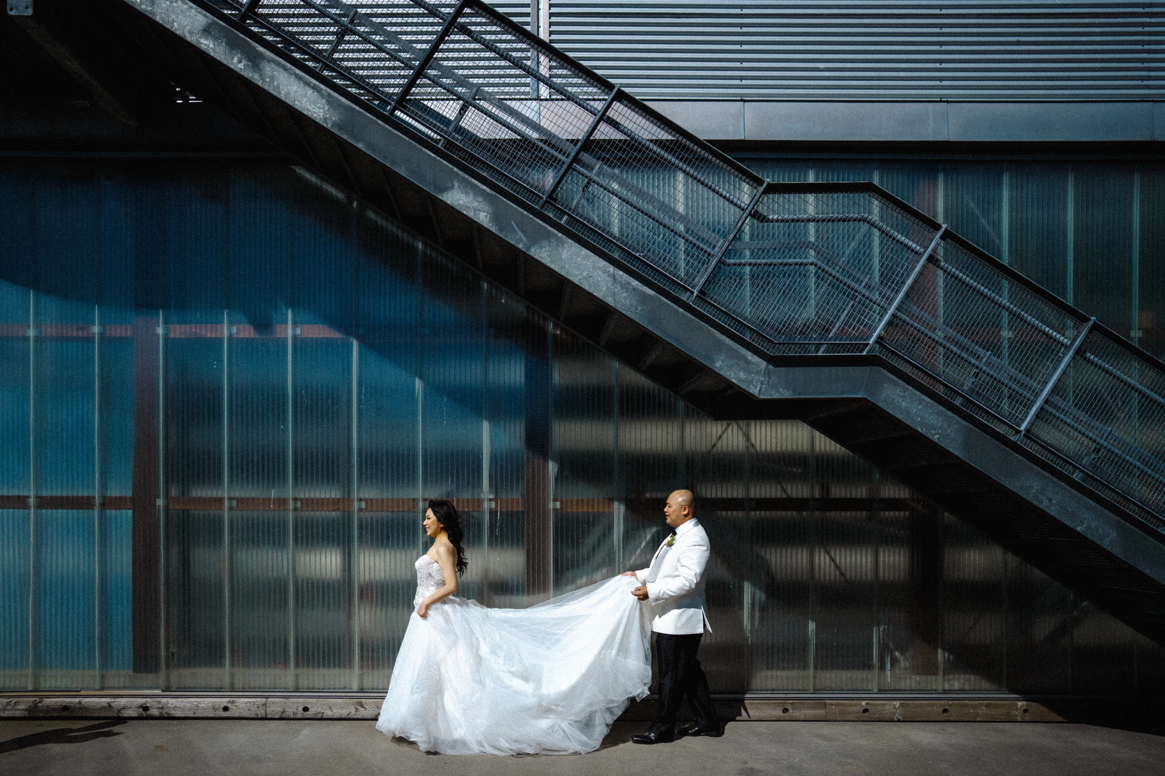 Groom helping the bride with her dress beneath the boathouse staircase.
