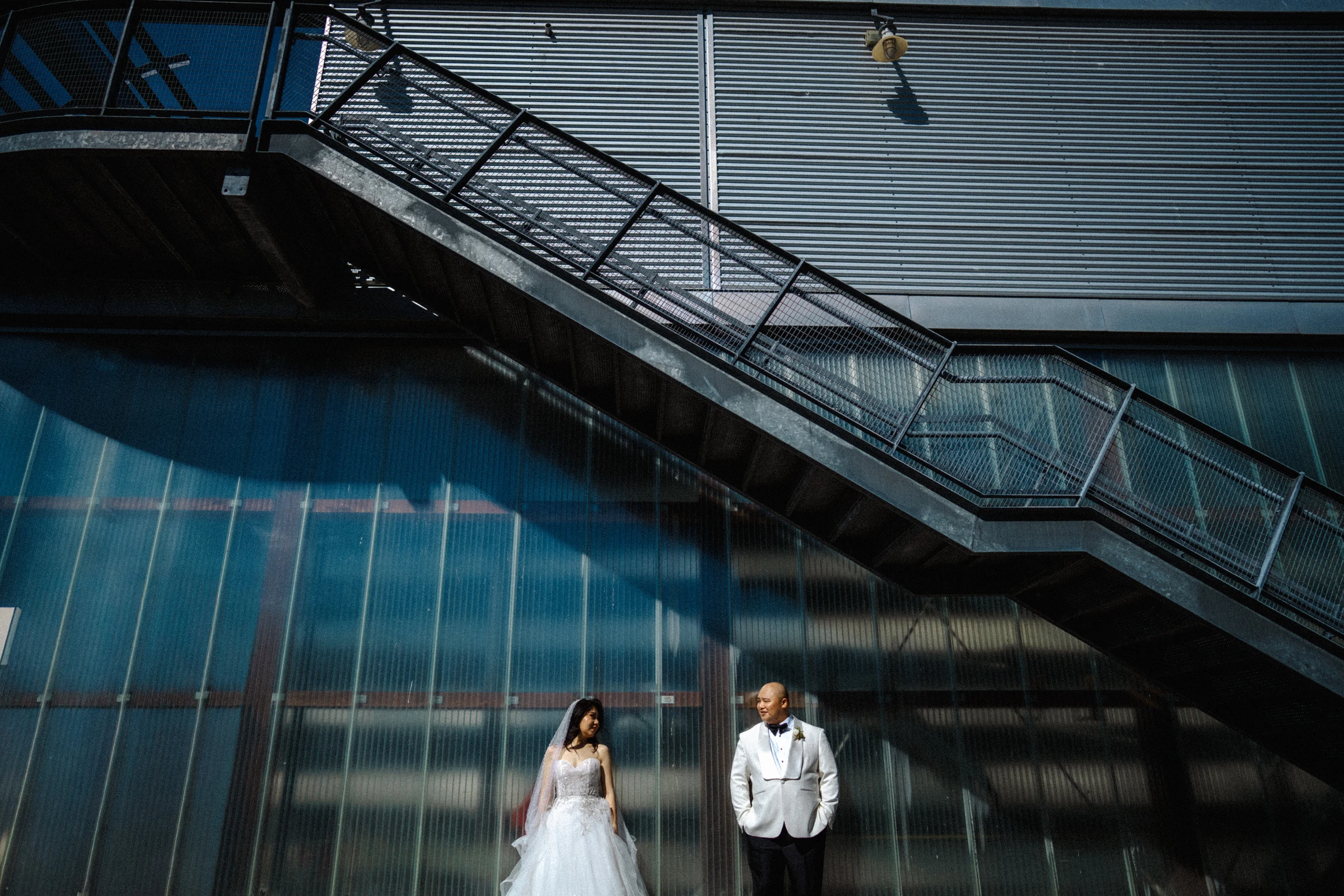 Wide portrait of the couple beneath the boathouse staircase.
