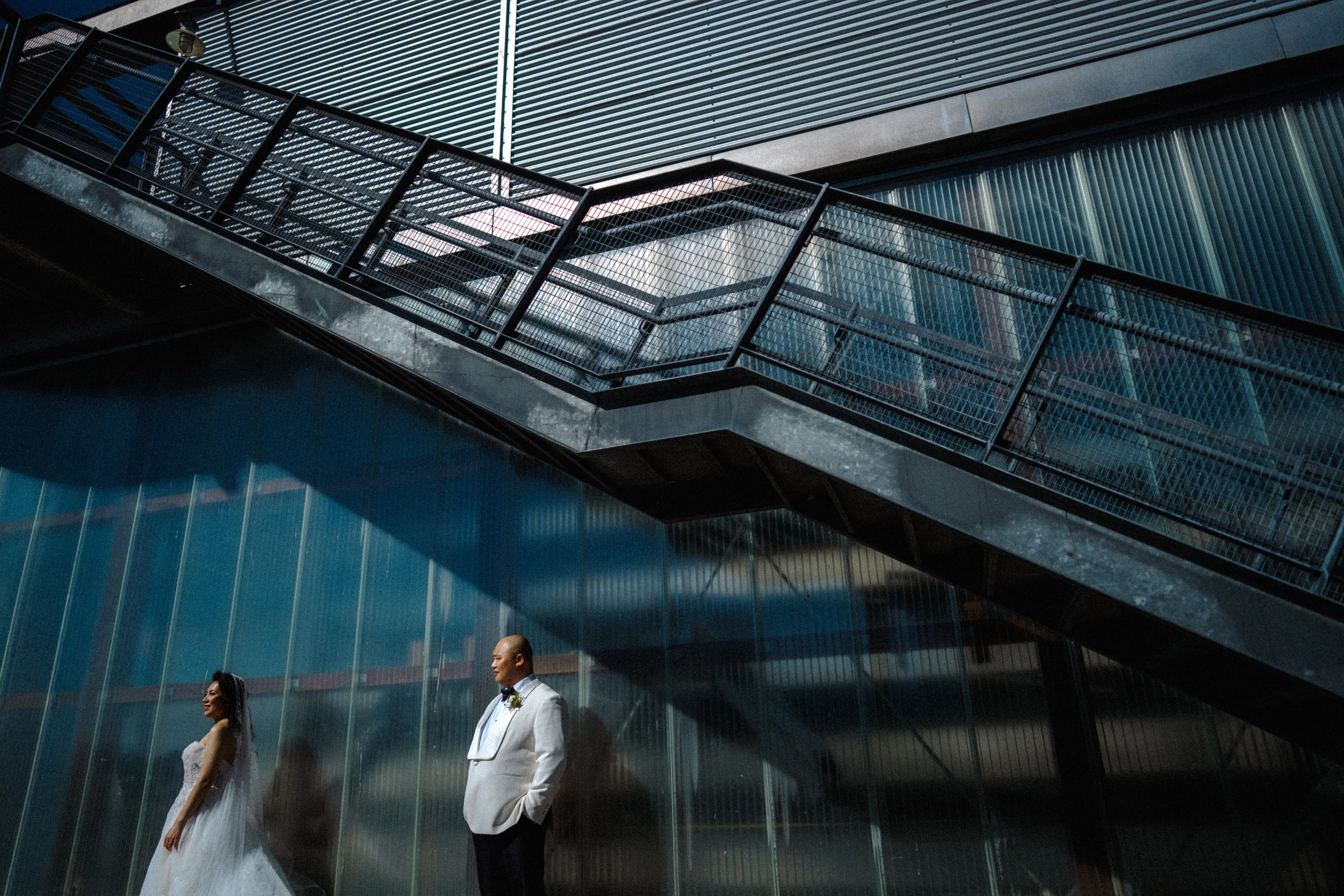 Couple standing beneath the metal stairs against the blue wall.