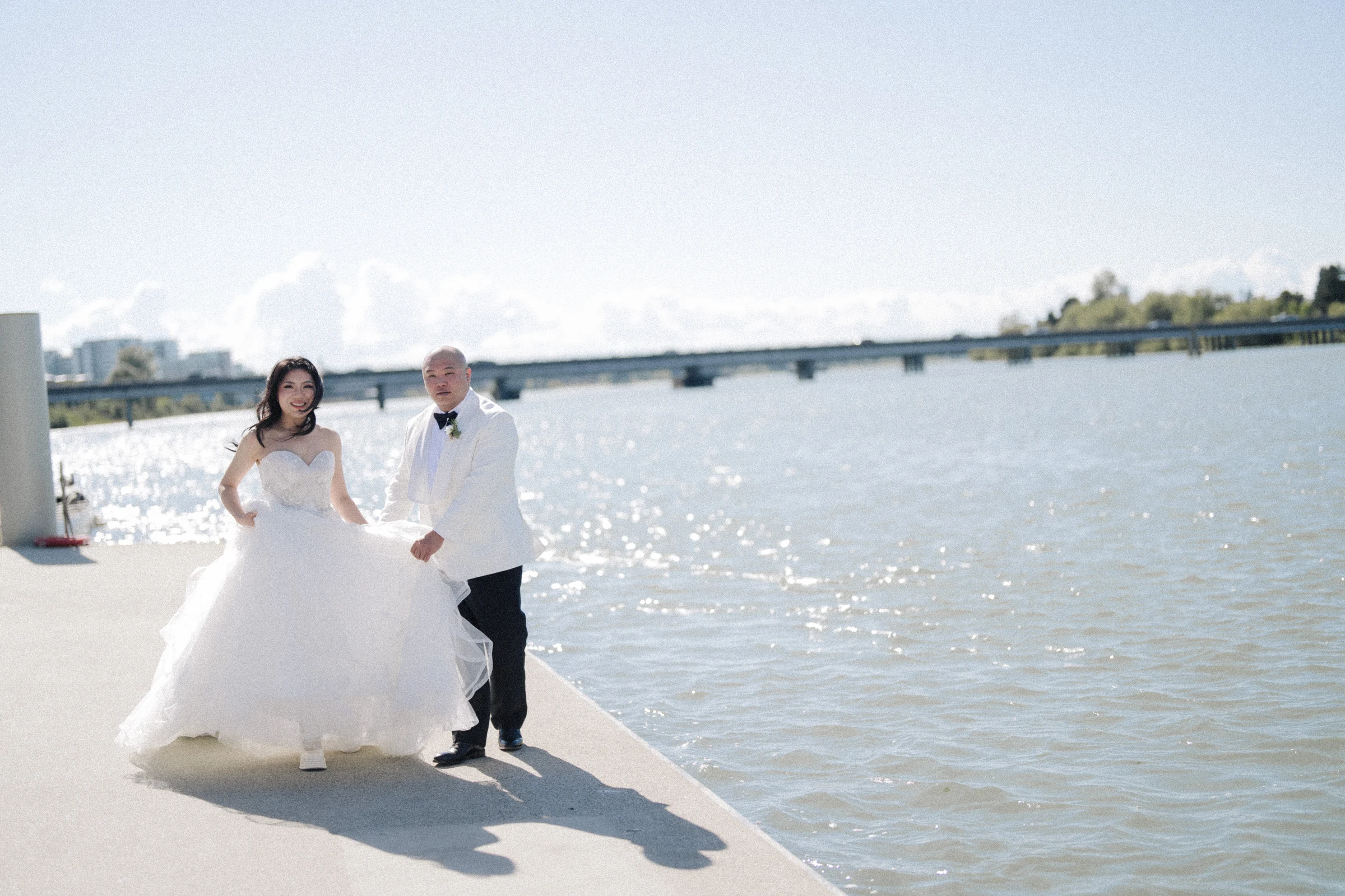 Couple moving together on the sunlit waterfront deck, with the wedding dress lifting.