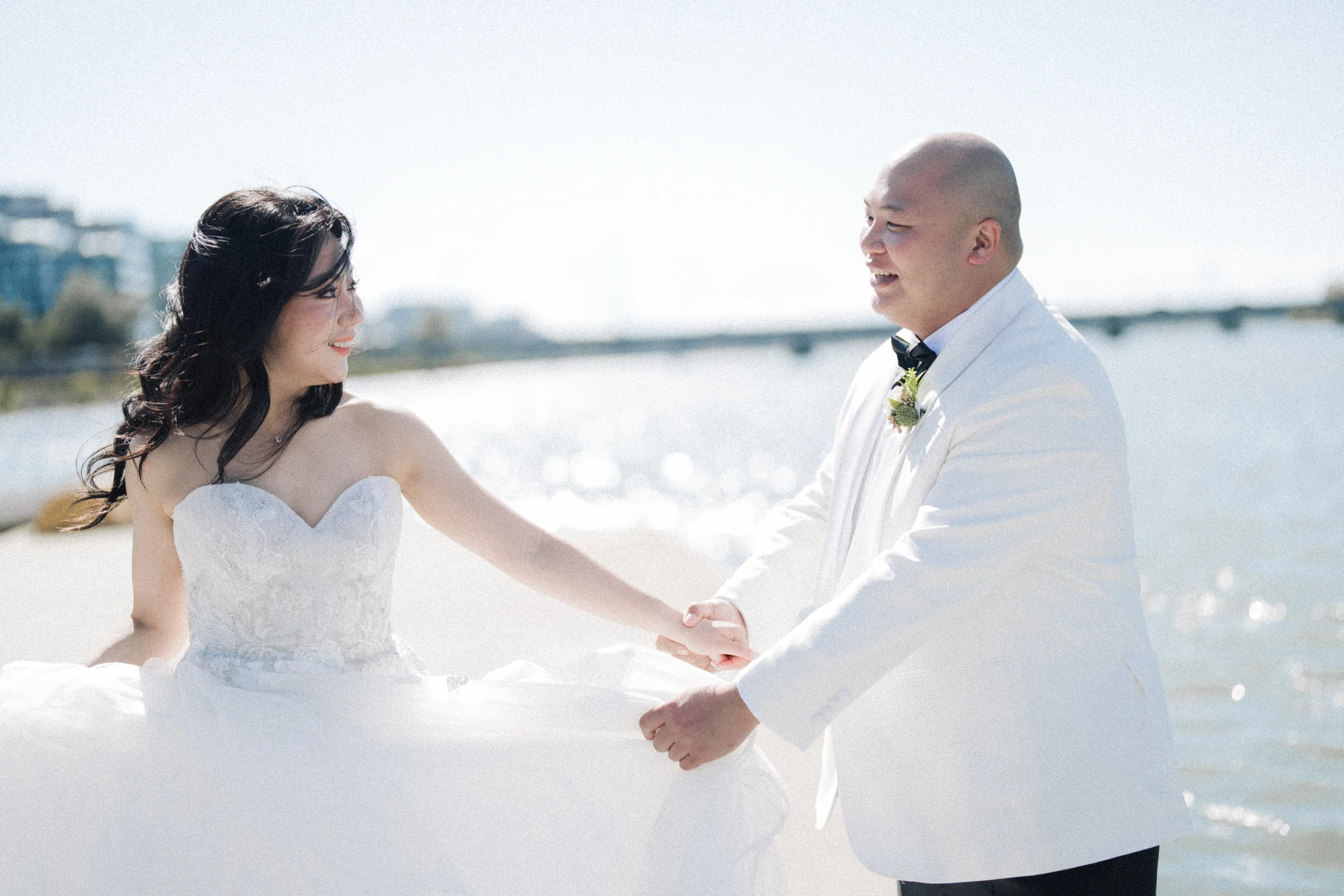Bride and groom holding hands and looking towards each other by the river.