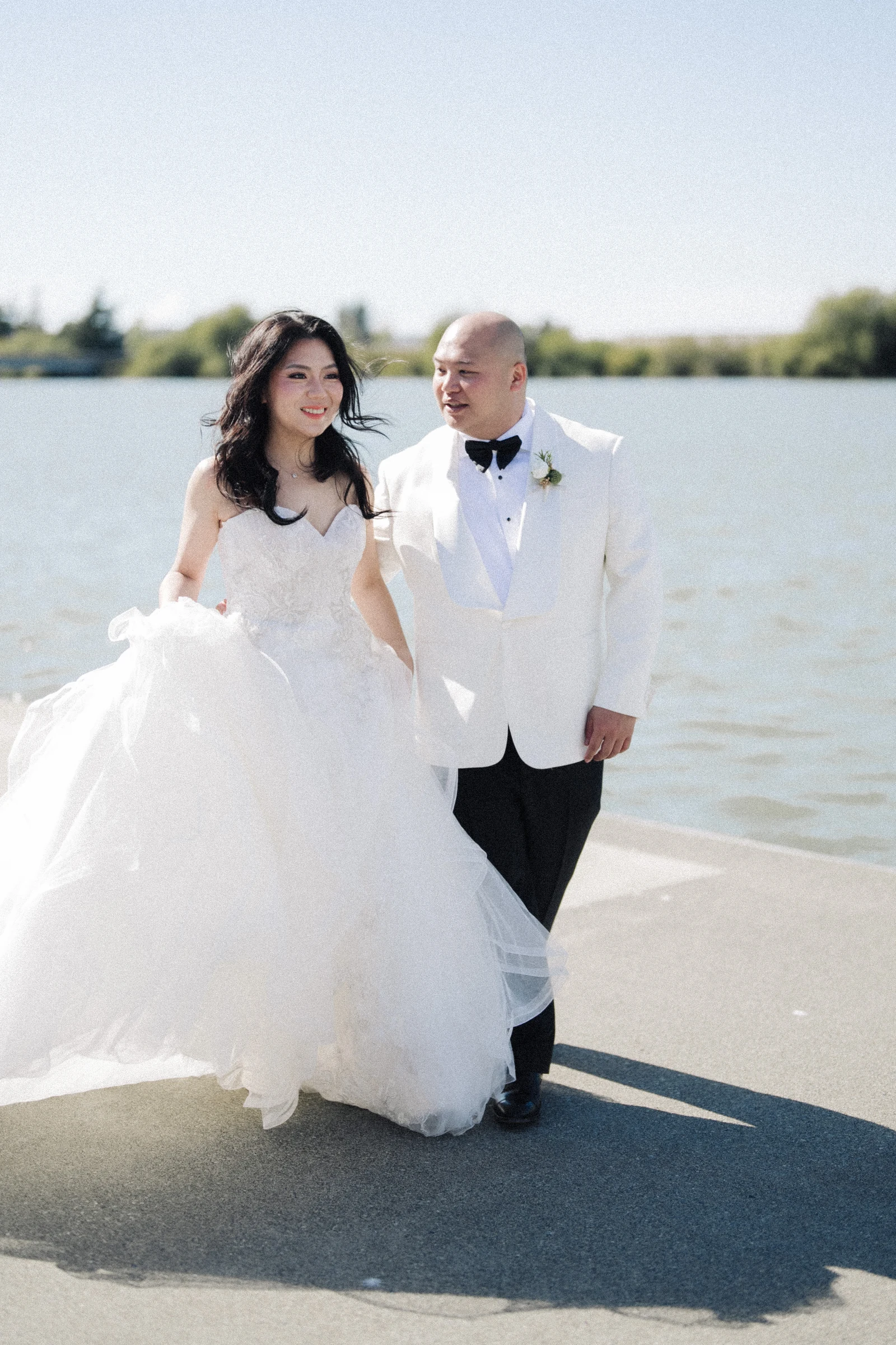 Couple standing together in bright light beside the water.