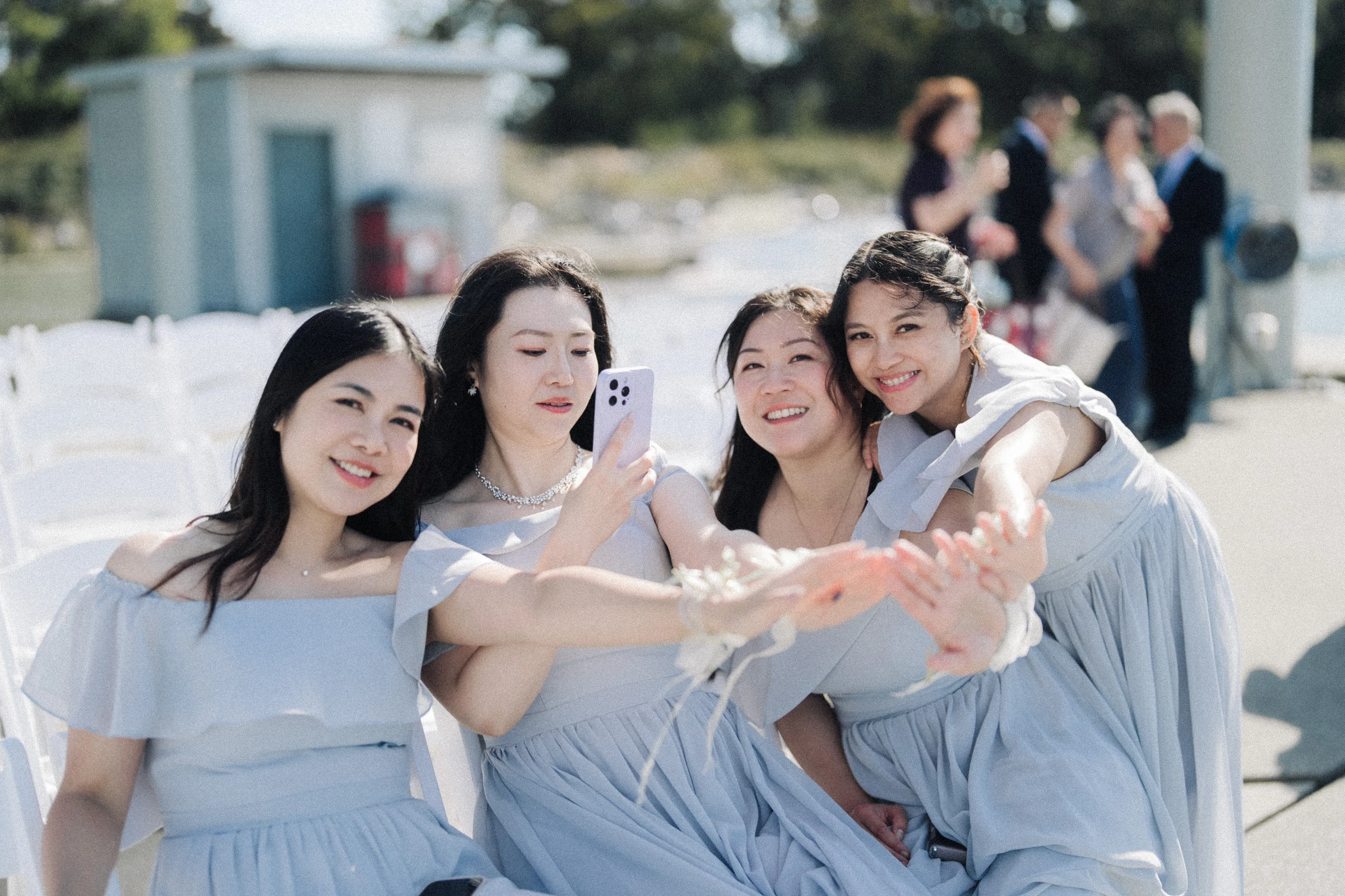 Bridesmaids in pale blue dresses leaning together for a waterfront portrait.
