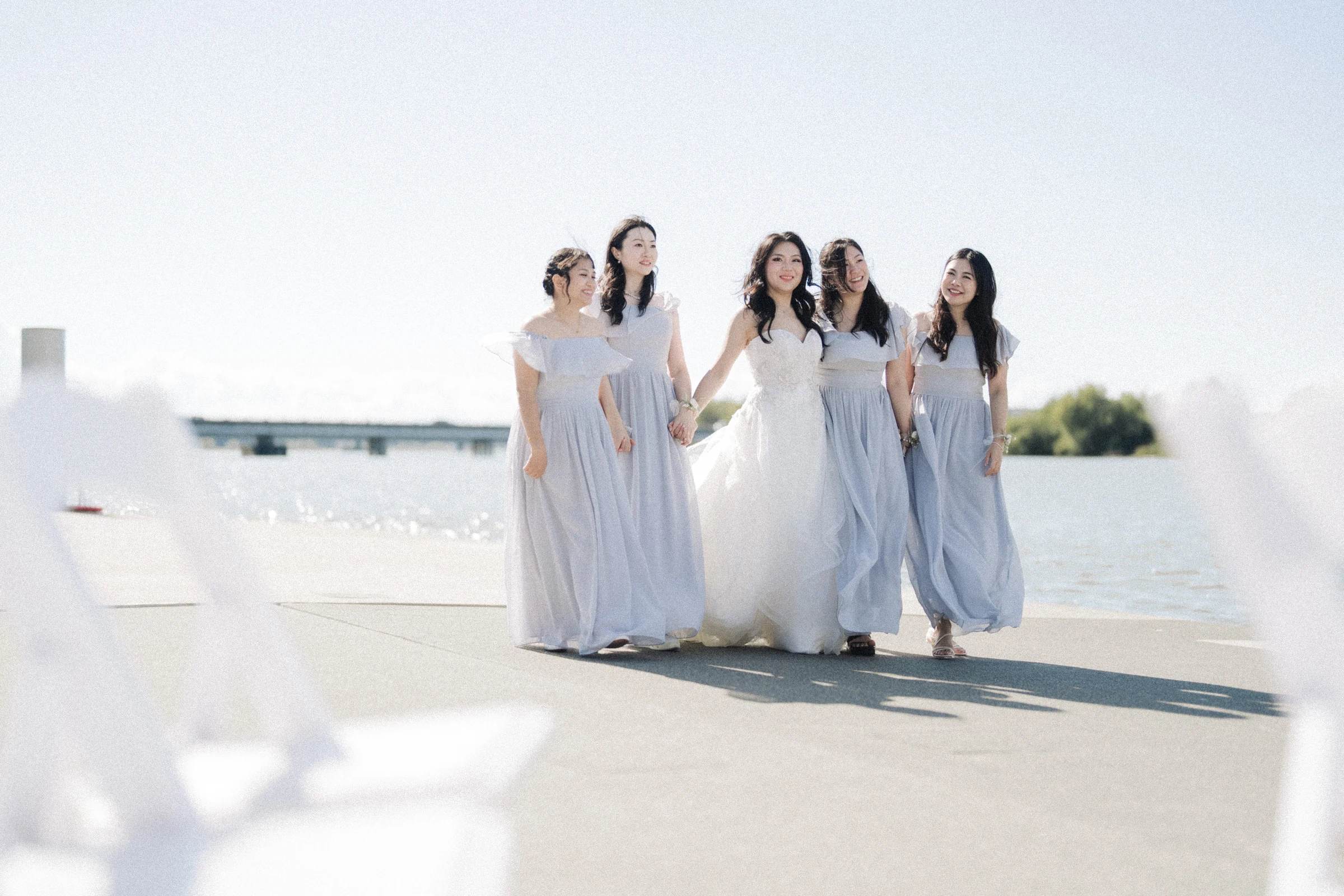 Bride and bridesmaids standing together against the bright river.