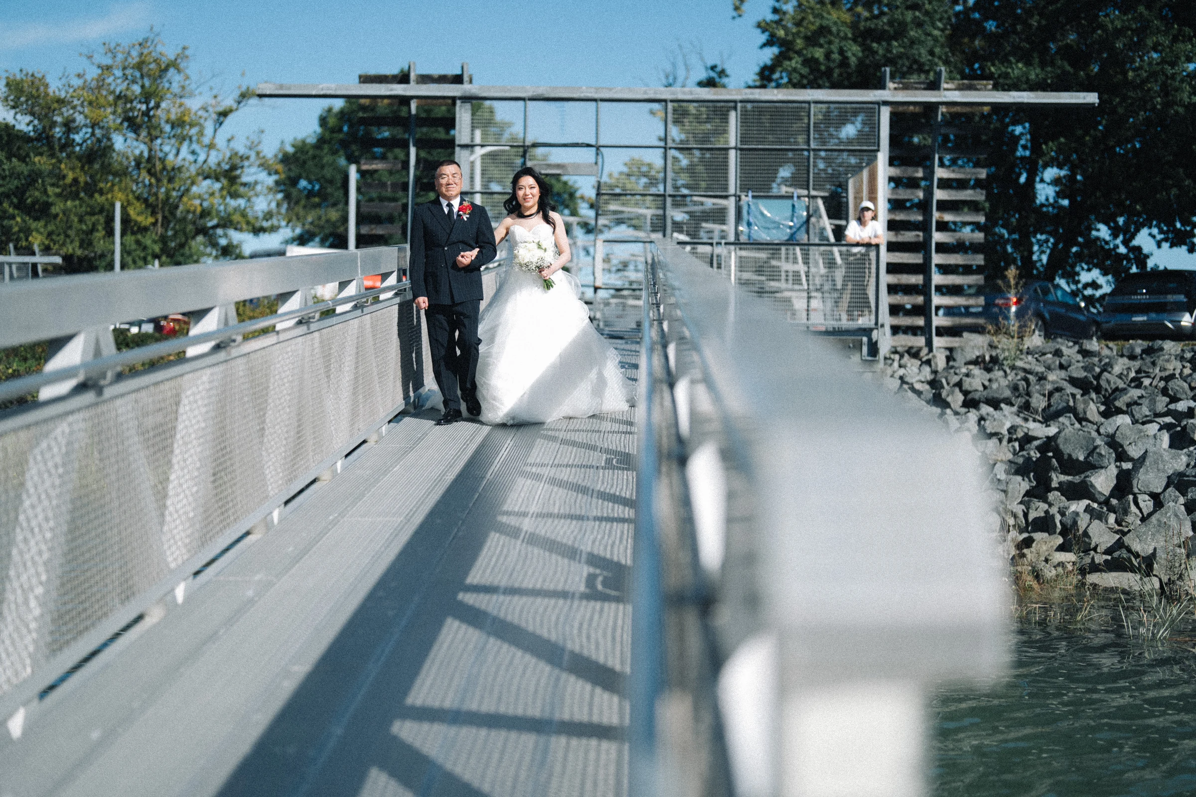 Bride walking along the raised boathouse walkway with a companion.