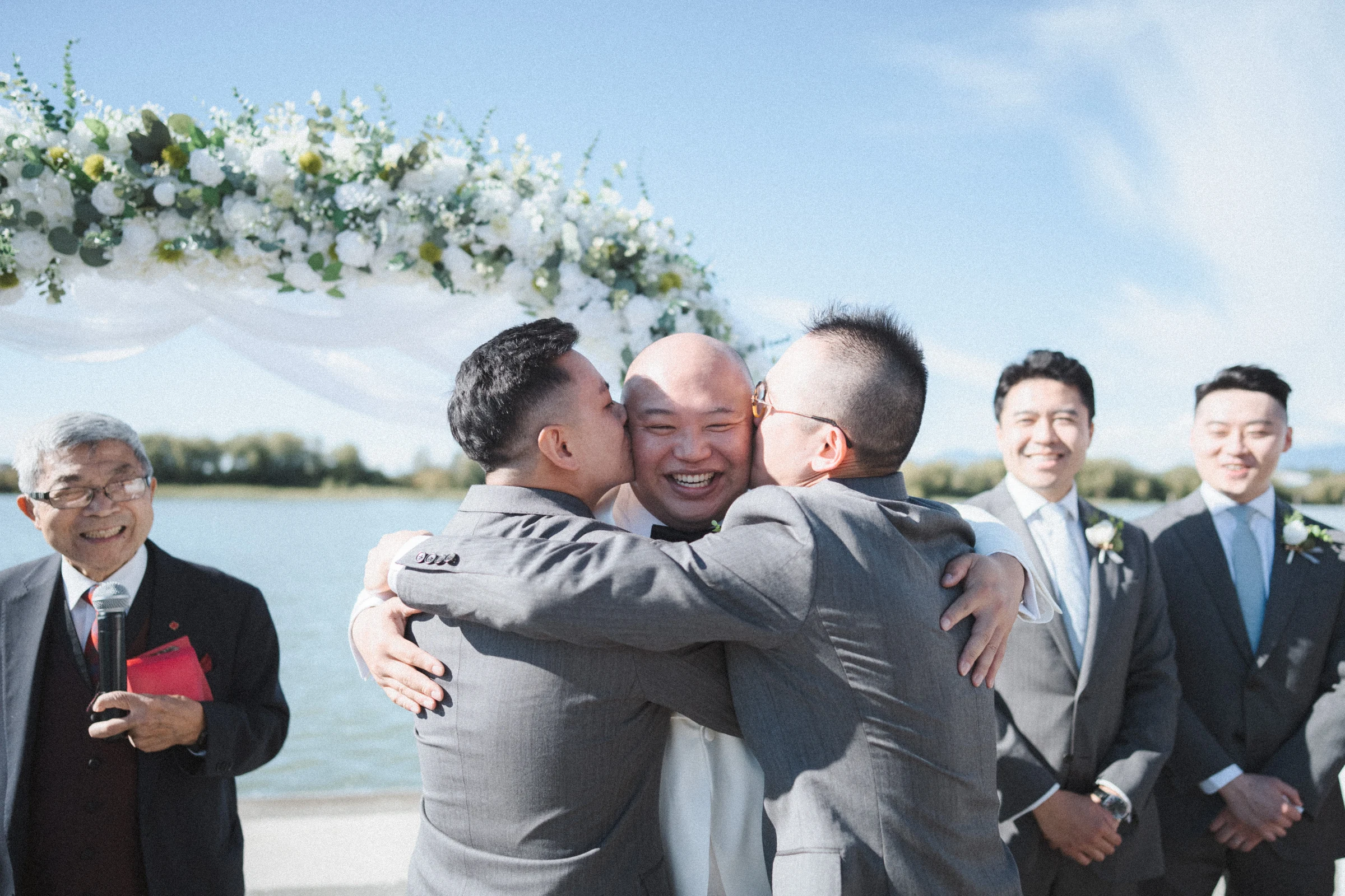 Groom embracing friends beside the flower arch.
