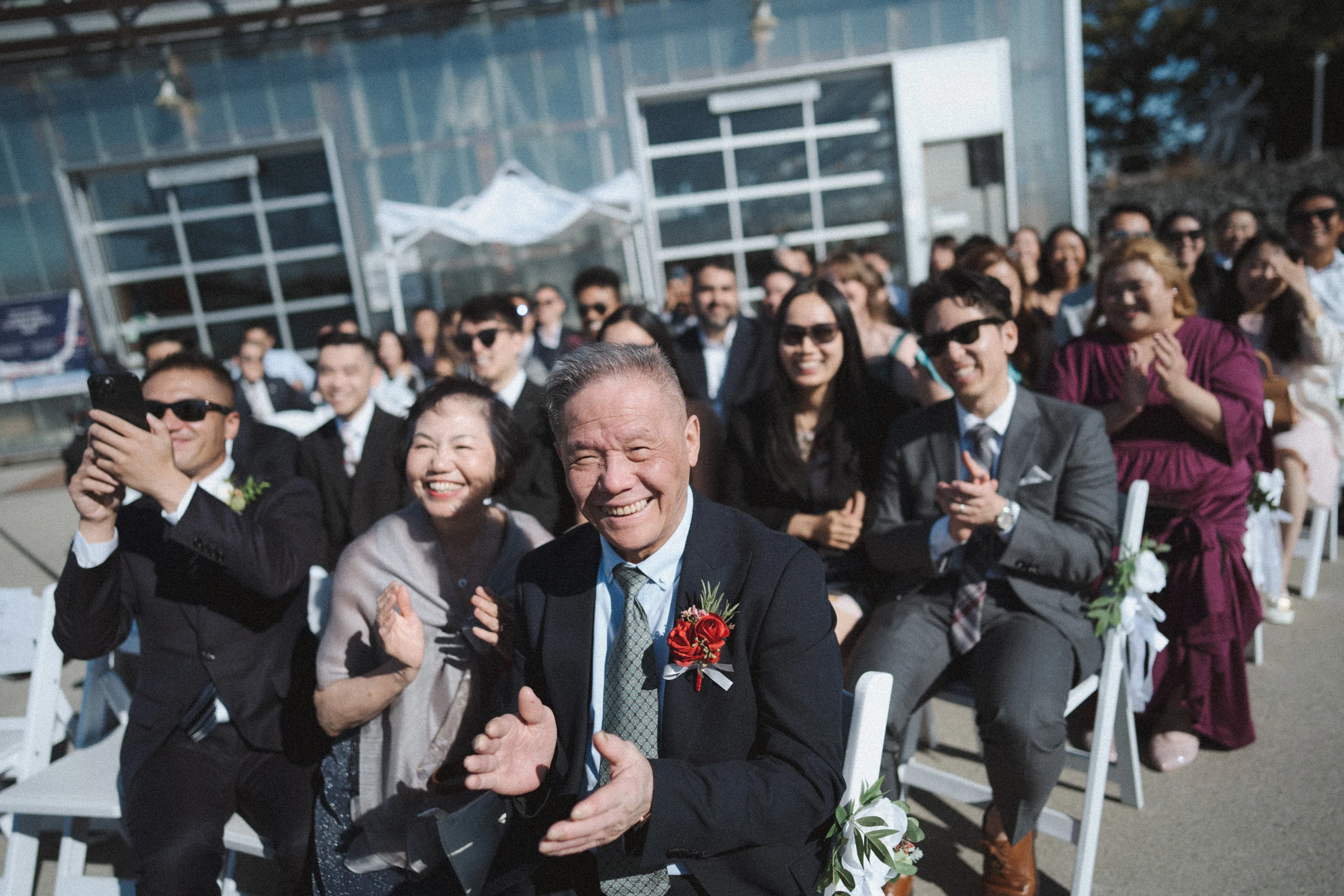 Guests smiling and raising phones from the ceremony chairs.