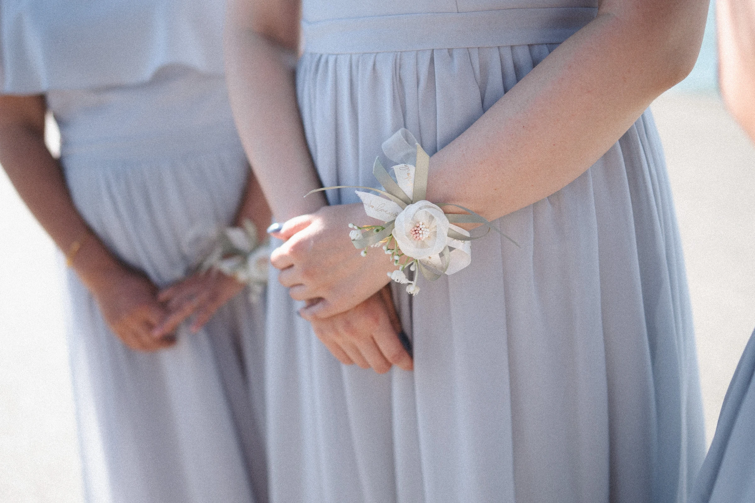Detail of bridesmaids' hands and white wrist flowers against pale blue dresses.