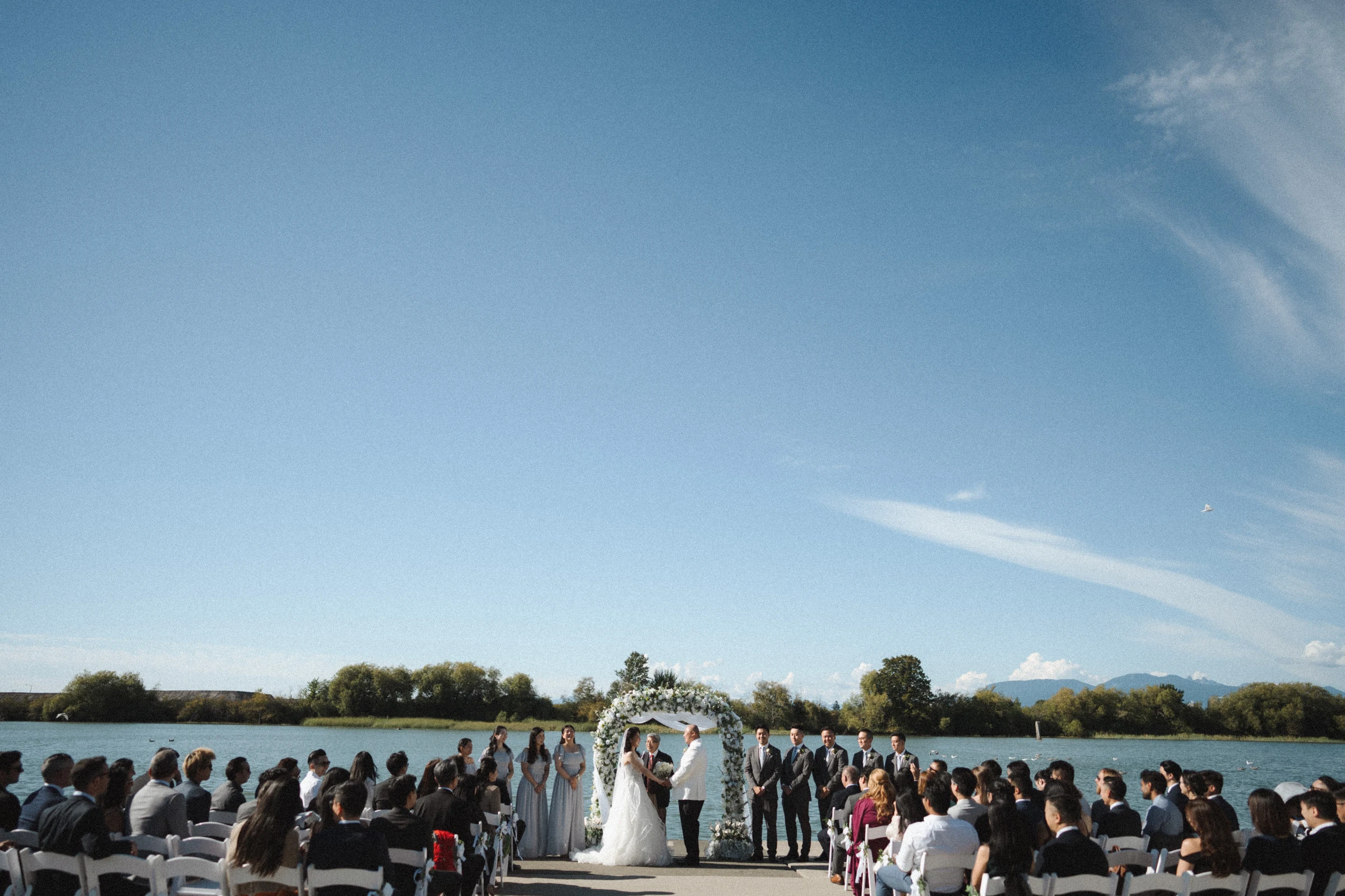 Wide view of the ceremony beside the river under a blue sky.