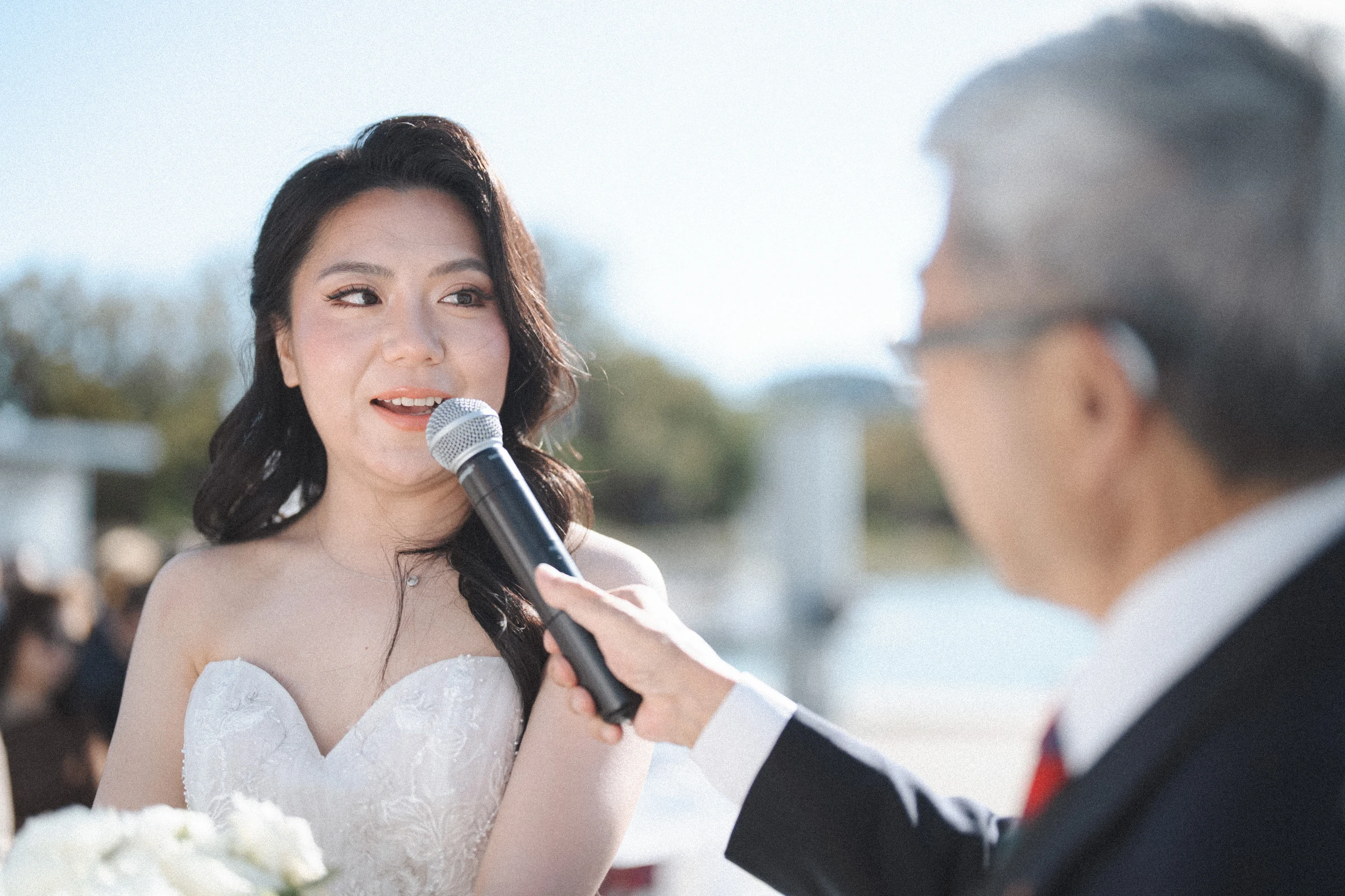 Bride speaking into a microphone while looking towards the groom.