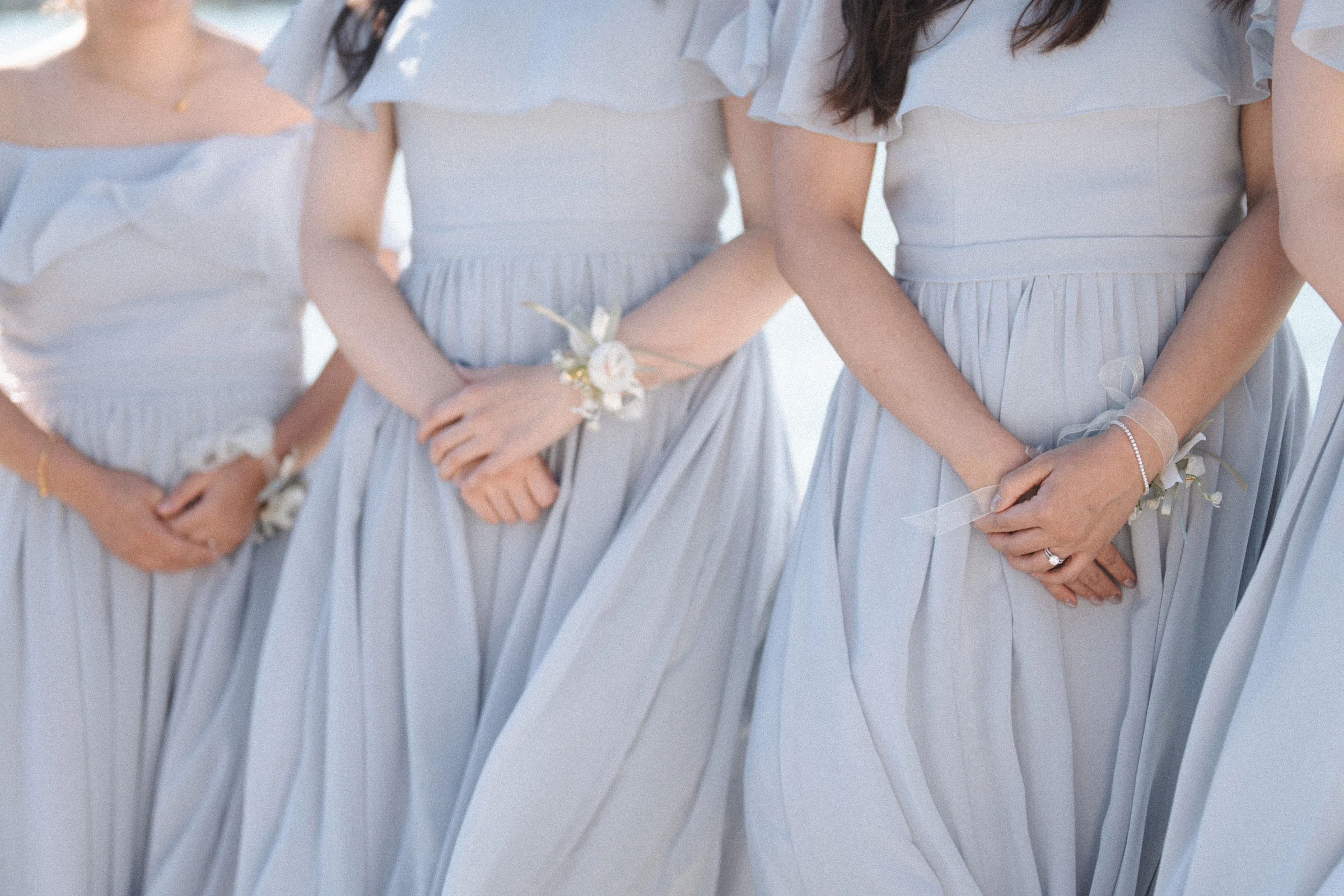 Detail of bridesmaids' hands resting against their pale blue dresses.
