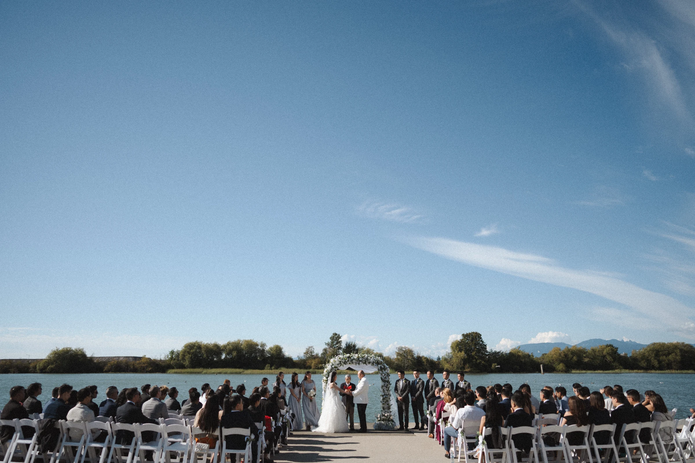Wide waterfront view of the couple beneath the flower arch.