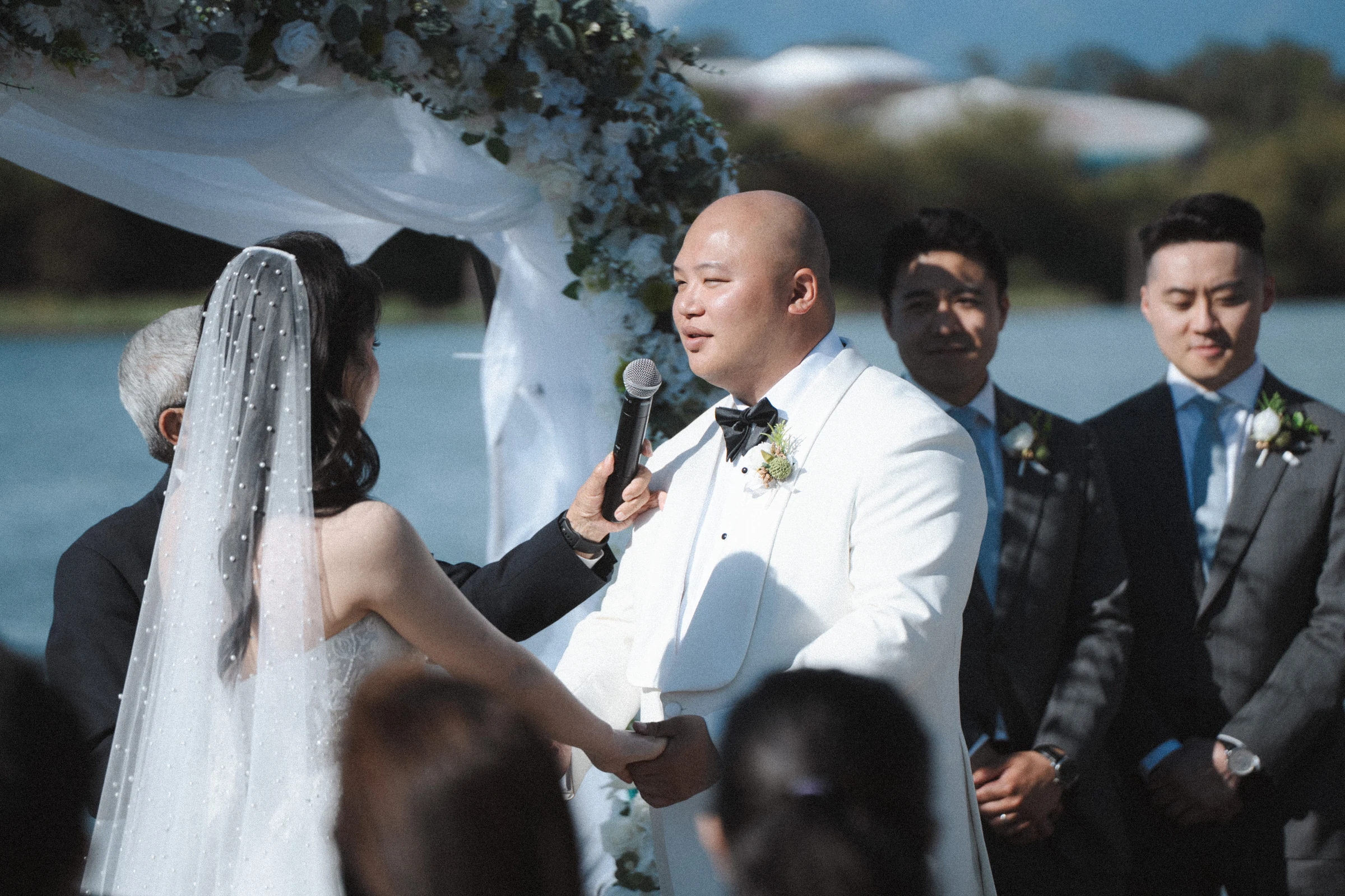Groom holding the microphone as the bride faces him beneath the arch.
