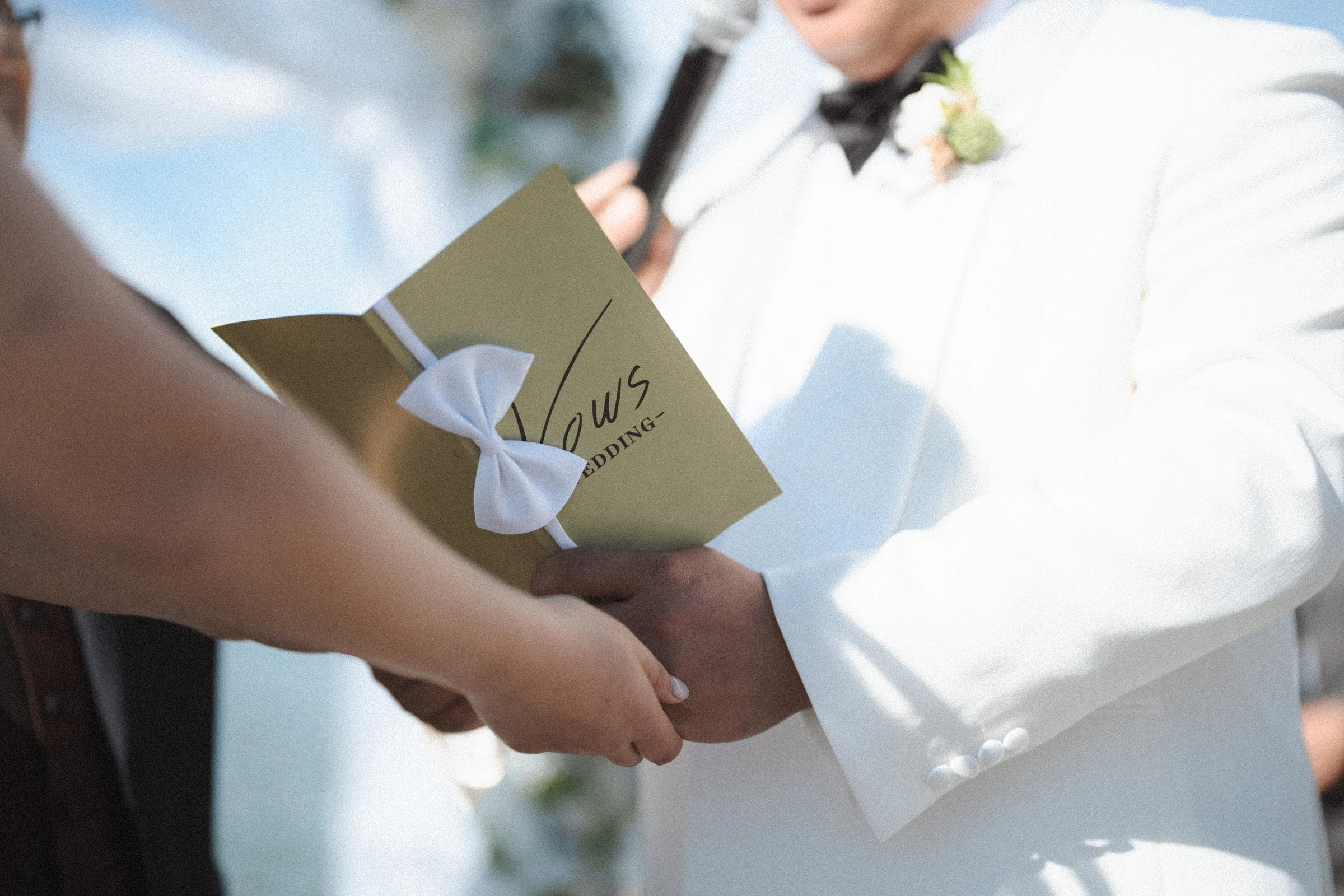 Close detail of a gold vow booklet and the couple's hands.