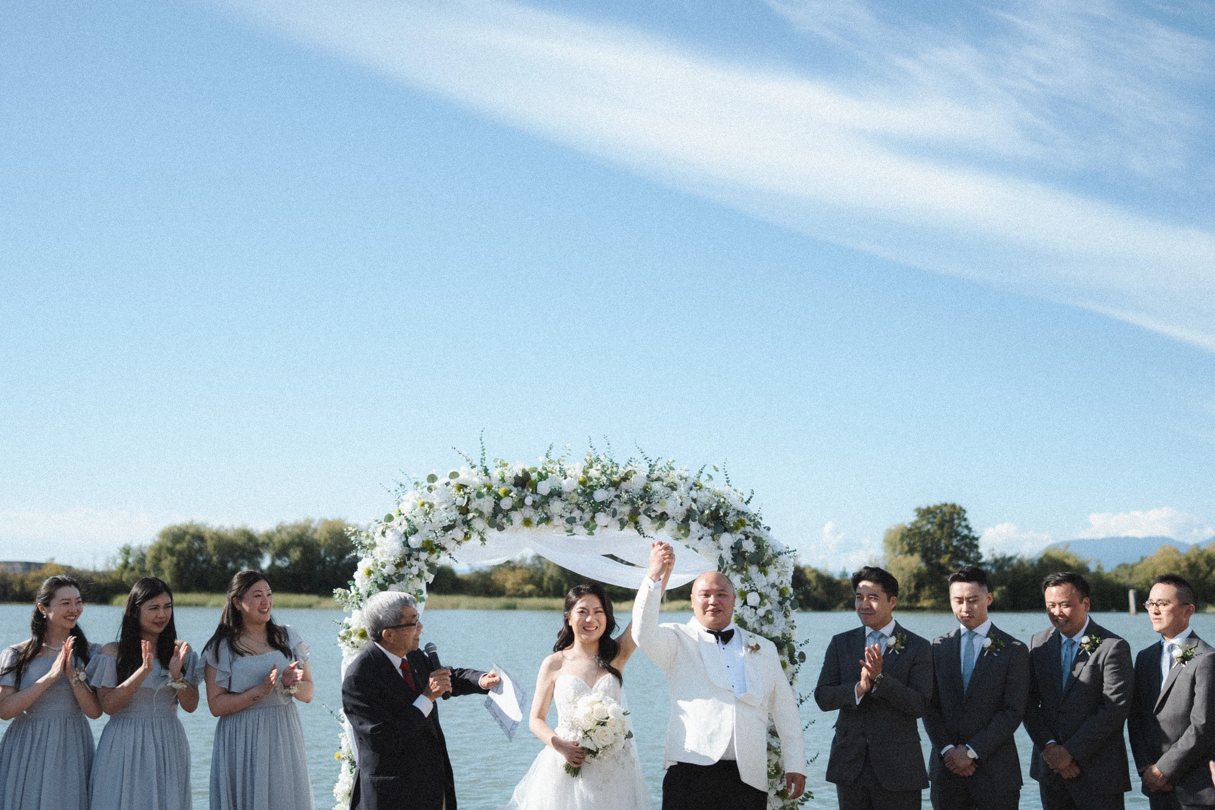 Couple and wedding party standing together beneath the ceremony arch.