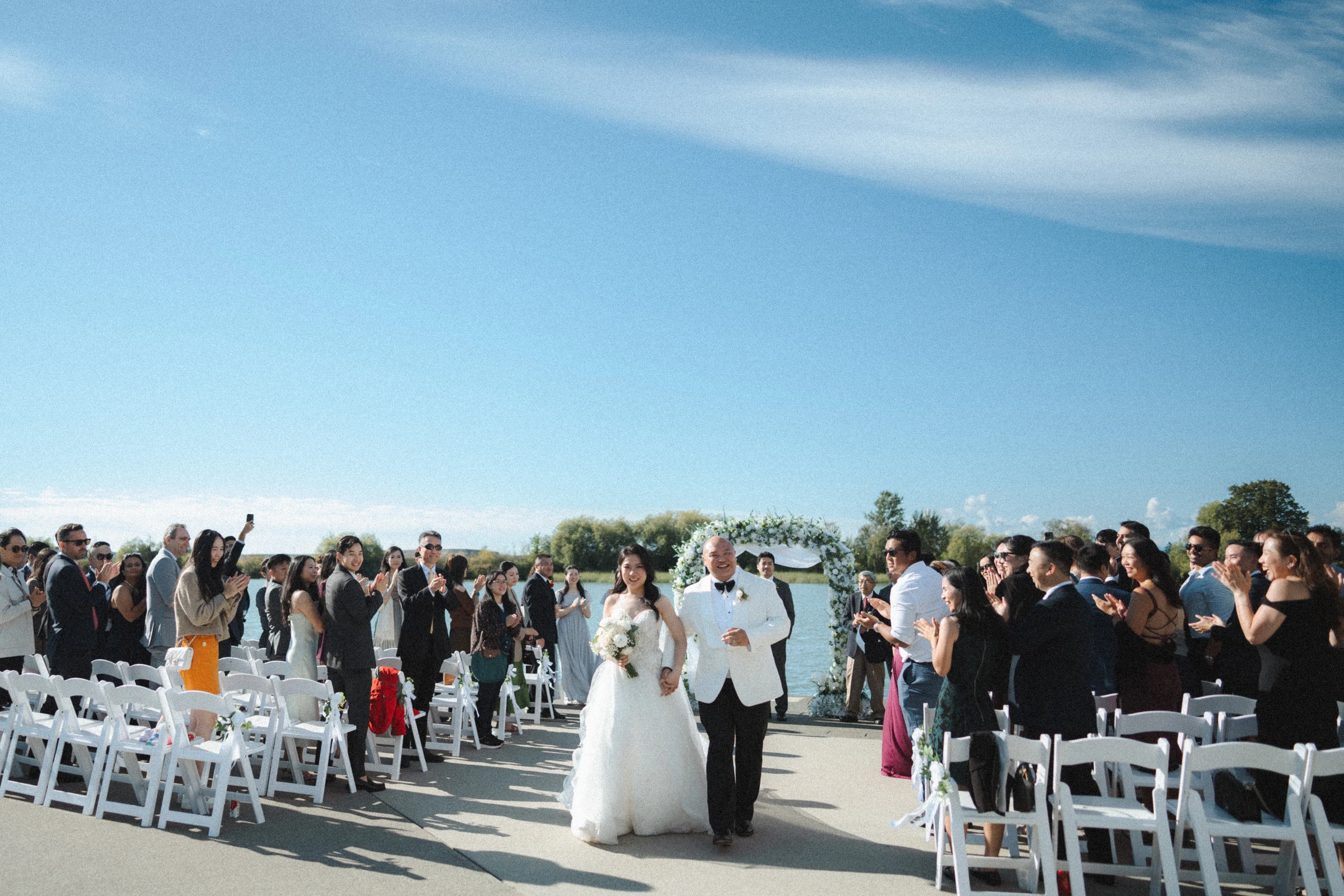 Newlyweds smiling as they walk between rows of applauding guests.