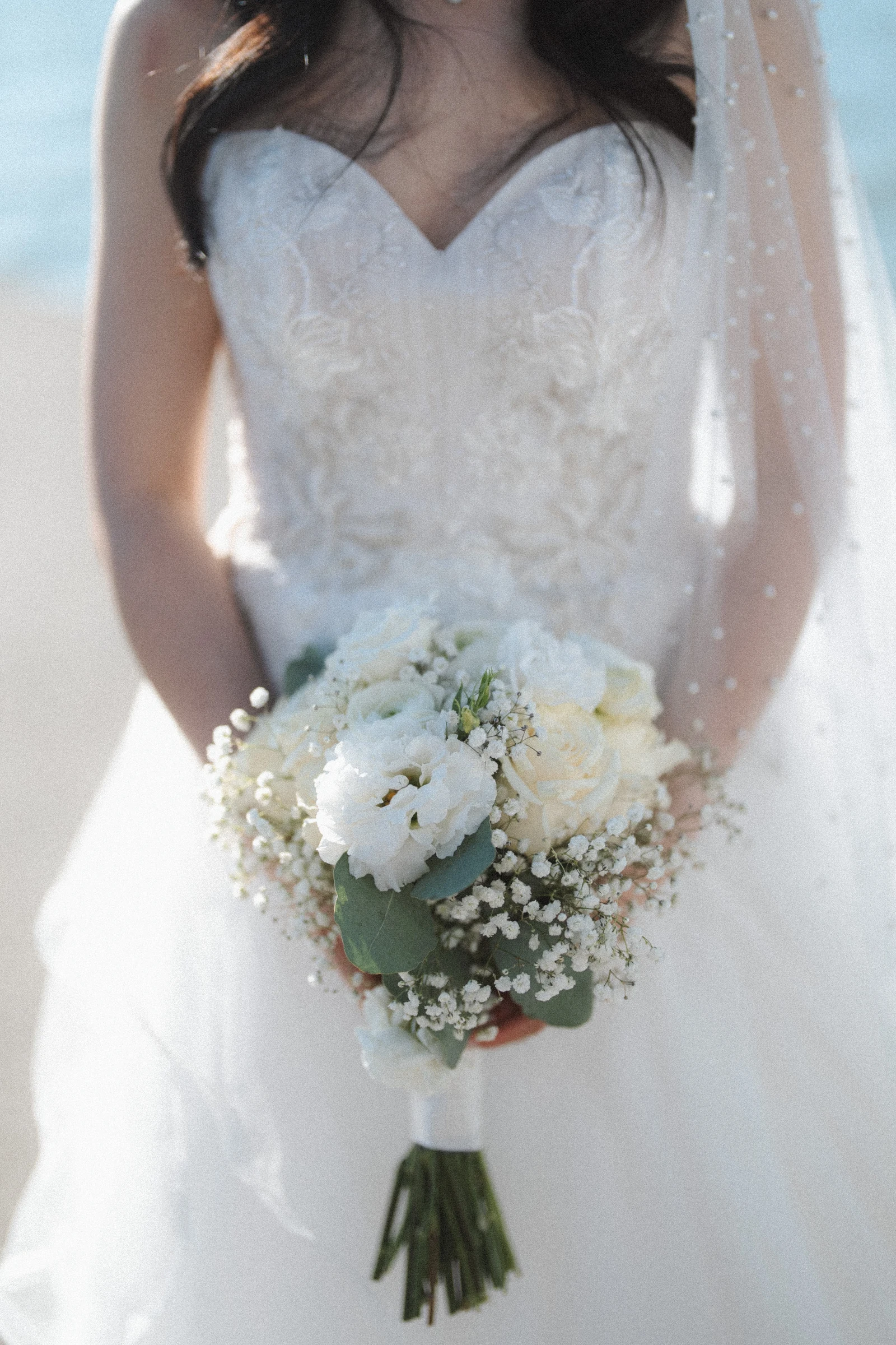 Detail of the bride's white dress and bouquet beside the water.