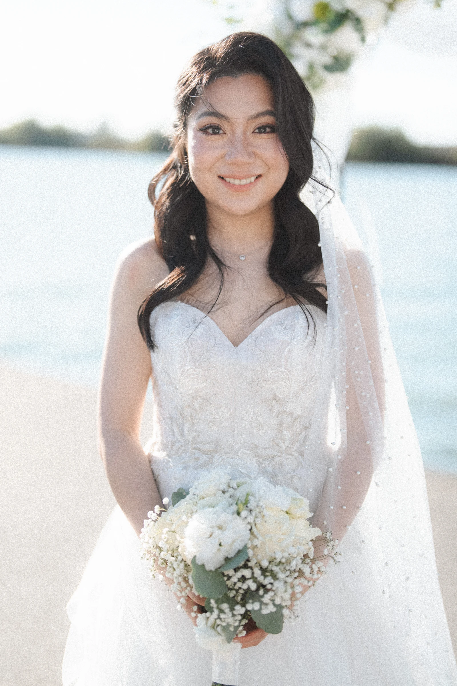 Bride smiling in a softly lit waterfront portrait.