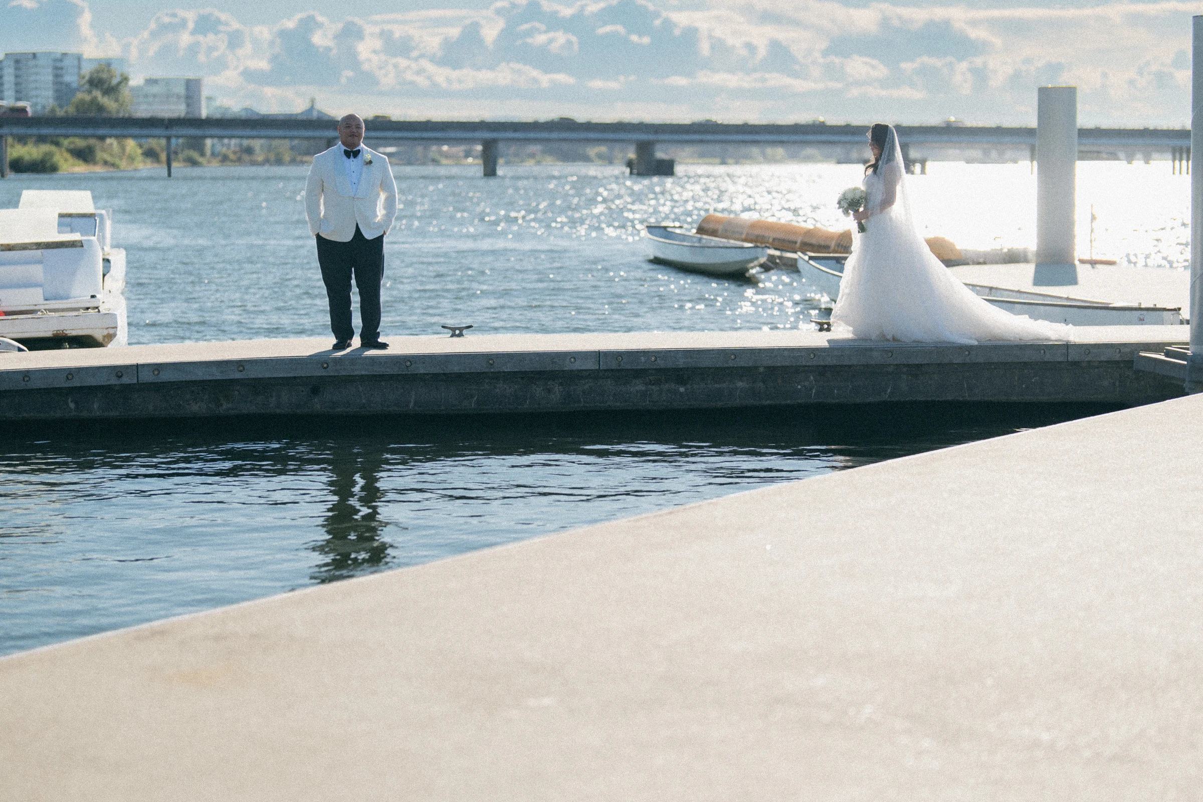 Couple standing apart on a narrow dock beside moored boats.
