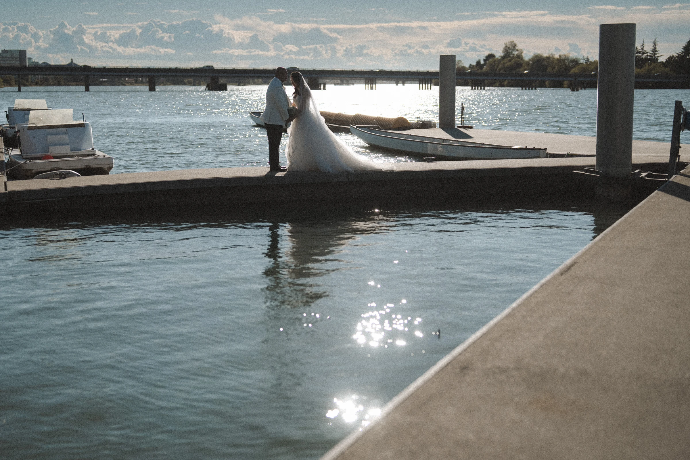 Couple standing on the dock with the bride's long train laid beside the water.